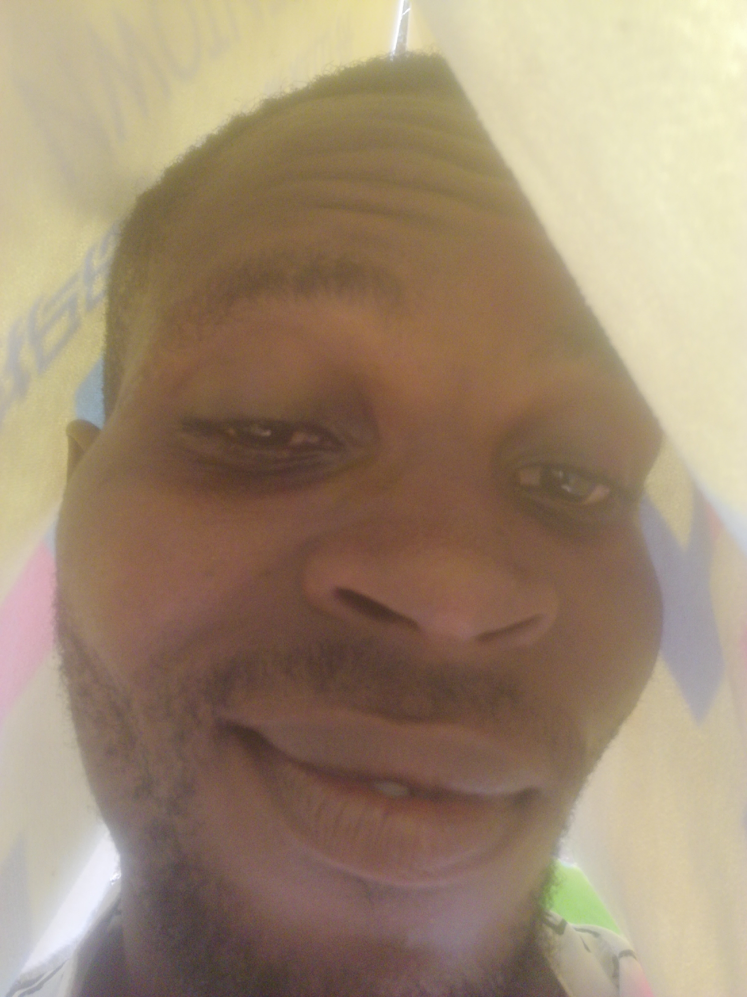 The image shows a close-up of a Black male's face, partially obscured by a light-colored material. The background is out of focus and appears to have some lettering. No location is discernible from the image.