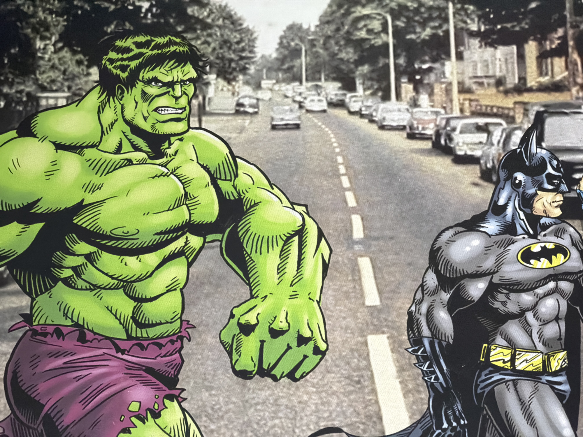The image presents two comic book characters, the Hulk and Batman, superimposed onto a photographic background depicting a residential street in Maidstone, United Kingdom.
On the left side of the frame, the Hulk is rendered in a vibrant green with distinct black outlines, characteristic of comic book artistry. He possesses a highly muscular physique, an angry facial expression with a furrowed brow and clenched teeth, and shaggy black hair. He is depicted wearing torn purple shorts. His posture suggests forward motion, with his left arm bent at the elbow and his right arm extended slightly forward. The artistic detailing includes cross-hatching to emphasize musculature and shadows.
On the right, Batman is depicted in profile, facing left towards the general direction of the Hulk. He is presented in a grey suit with a black cowl, cape, and gauntlets, accented by a prominent yellow utility belt with discernible compartments. A black bat symbol is visible on his chest. His posture is upright and appears watchful. Similar to the Hulk, he is rendered in a comic book style with dark outlines and shading details.
The background is a photograph of an asphalt road, marked by dashed white lines indicating a central division or lane separation. The road gently curves to the left as it recedes into the distance. Numerous vehicles, predominantly older model sedans, are parked along both sides of the street, with additional vehicles visible further down the road. Deciduous trees with substantial foliage line both sides of the street, partially obscuring multi-story residential buildings behind them. The overall lighting suggests an overcast or diffused daylight. The photographic background exhibits a desaturated color palette, which contrasts with the vivid primary and secondary colors of the superimposed characters.
The characters are placed within the scene but do not display direct interaction with each other or the environment. Their poses are static relative to the background, suggesting they are illustrative elements within the photographic scene.