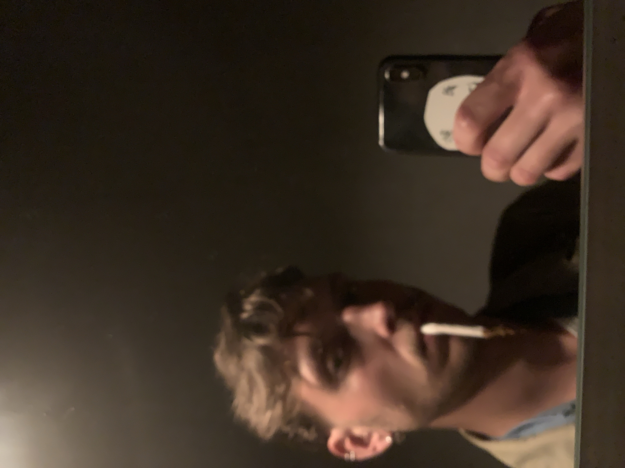 A man is taking a selfie in a mirror. He is holding a smartphone with a white pop socket on the back. The reflection shows the man has short, curly hair, a beard, and an earring. There is no evidence to suggest the location is Tel-Aviv, Israel.