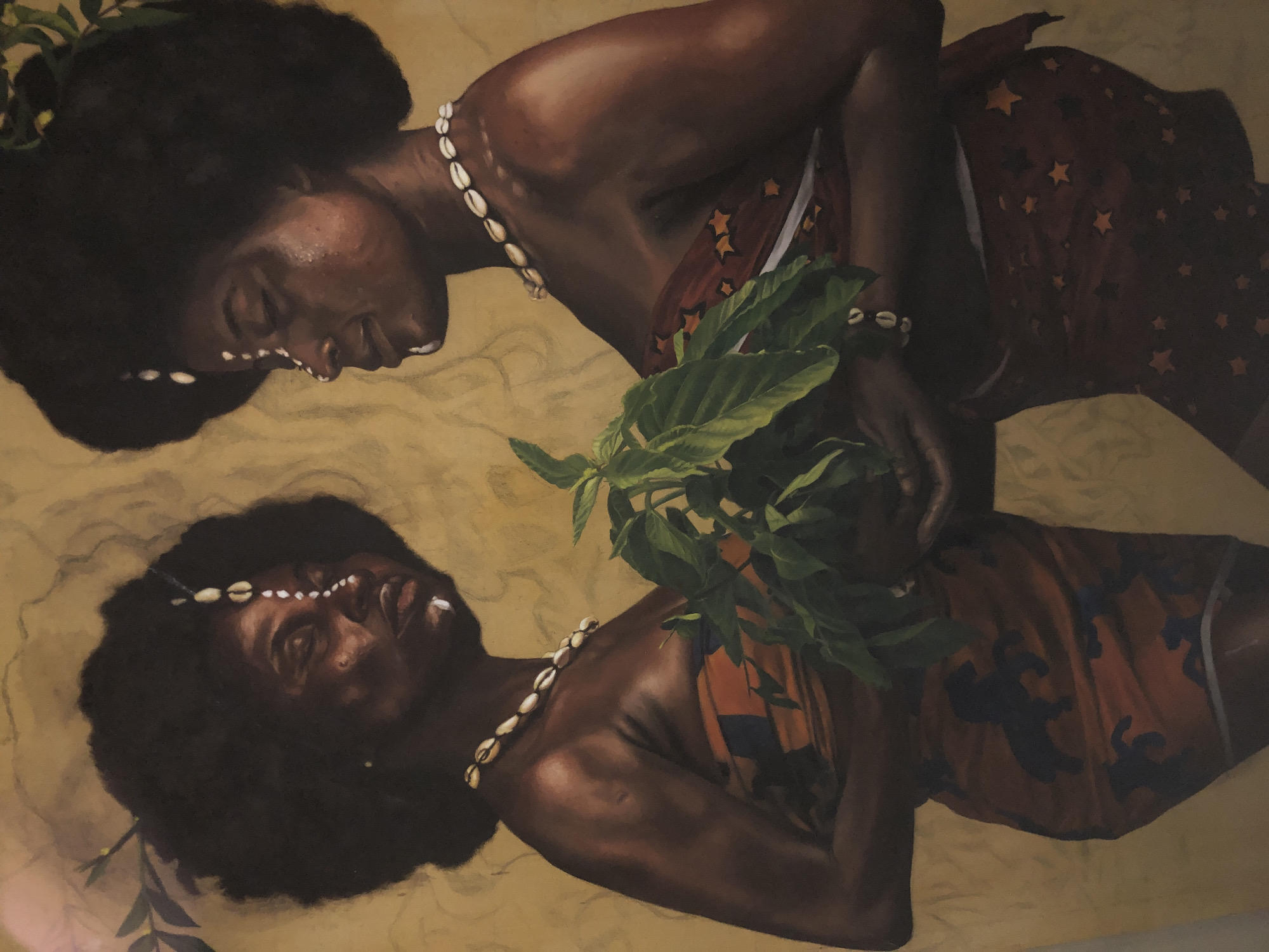 The painting depicts two Black women with voluminous dark afros, adorned with cowrie shell necklaces and white facial markings. Both women are facing each other, with their heads tilted slightly, and are holding a lush green plant with large leaves. The woman on the left is looking forward, while the woman on the right is looking down at the plant. Both women are wearing patterned fabrics around their lower bodies, one with a design of dark horses on an orange background, and the other with a pattern of orange stars on a dark background. The background is a textured, muted yellow, with faint vine-like elements and what appear to be subtle vine-like markings. The overall lighting suggests a warm, diffused natural light source. The style is realistic, with a focus on rendering skin tones and textures. The scene does not depict any specific location in the city of Ado, Nigeria.