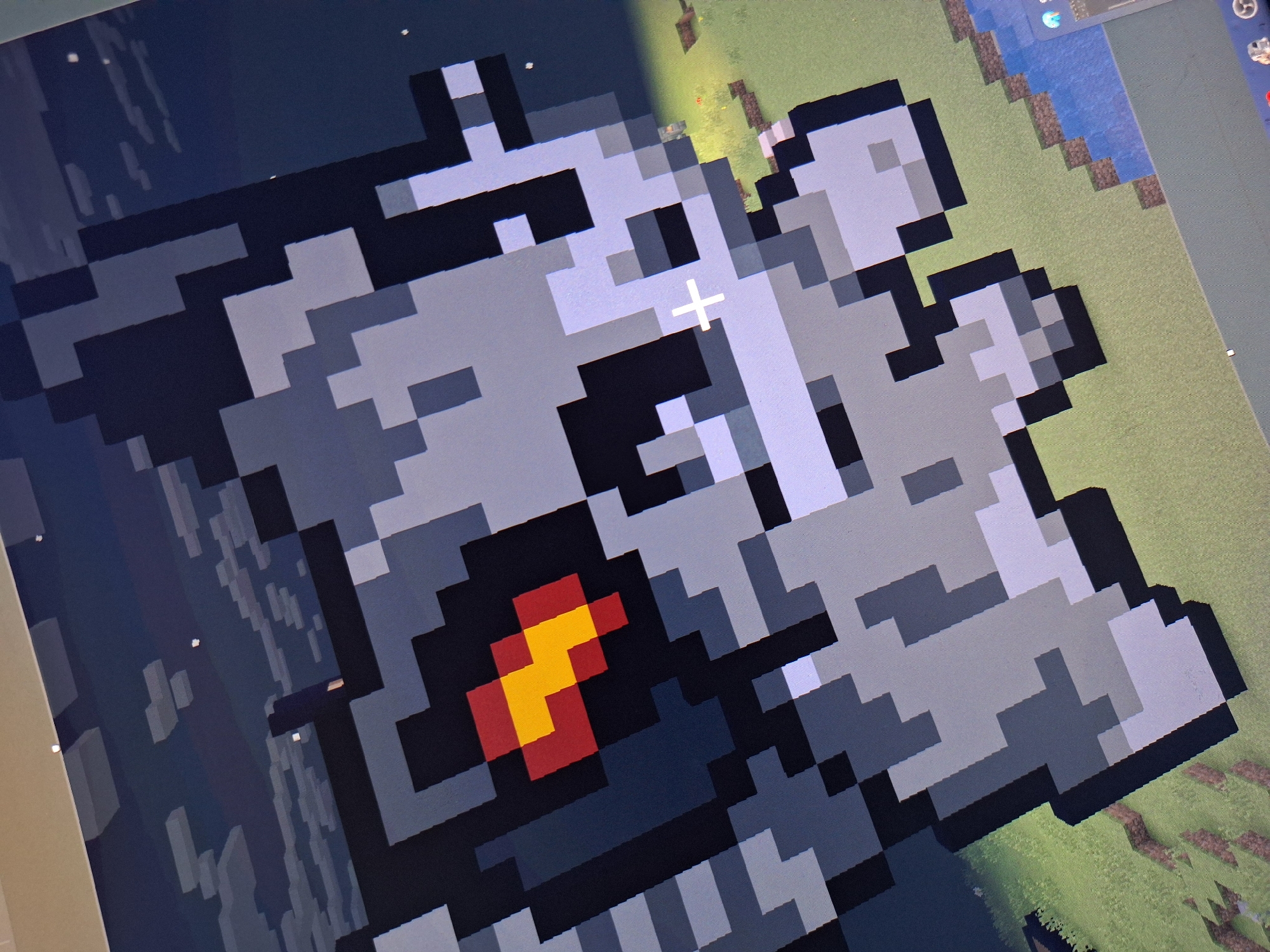 The image shows a close-up, pixelated view of a character from a video game, possibly Minecraft. The character appears to be a grey, robotic-like figure with a glowing red and yellow eye. It is set against a background that transitions from a dark, cloudy sky to a green, grassy landscape with water and brown terrain. There is a white crosshair visible on the character's face, suggesting it is a viewpoint within the game. The scene is not located in the city of Varna, Bulgaria.