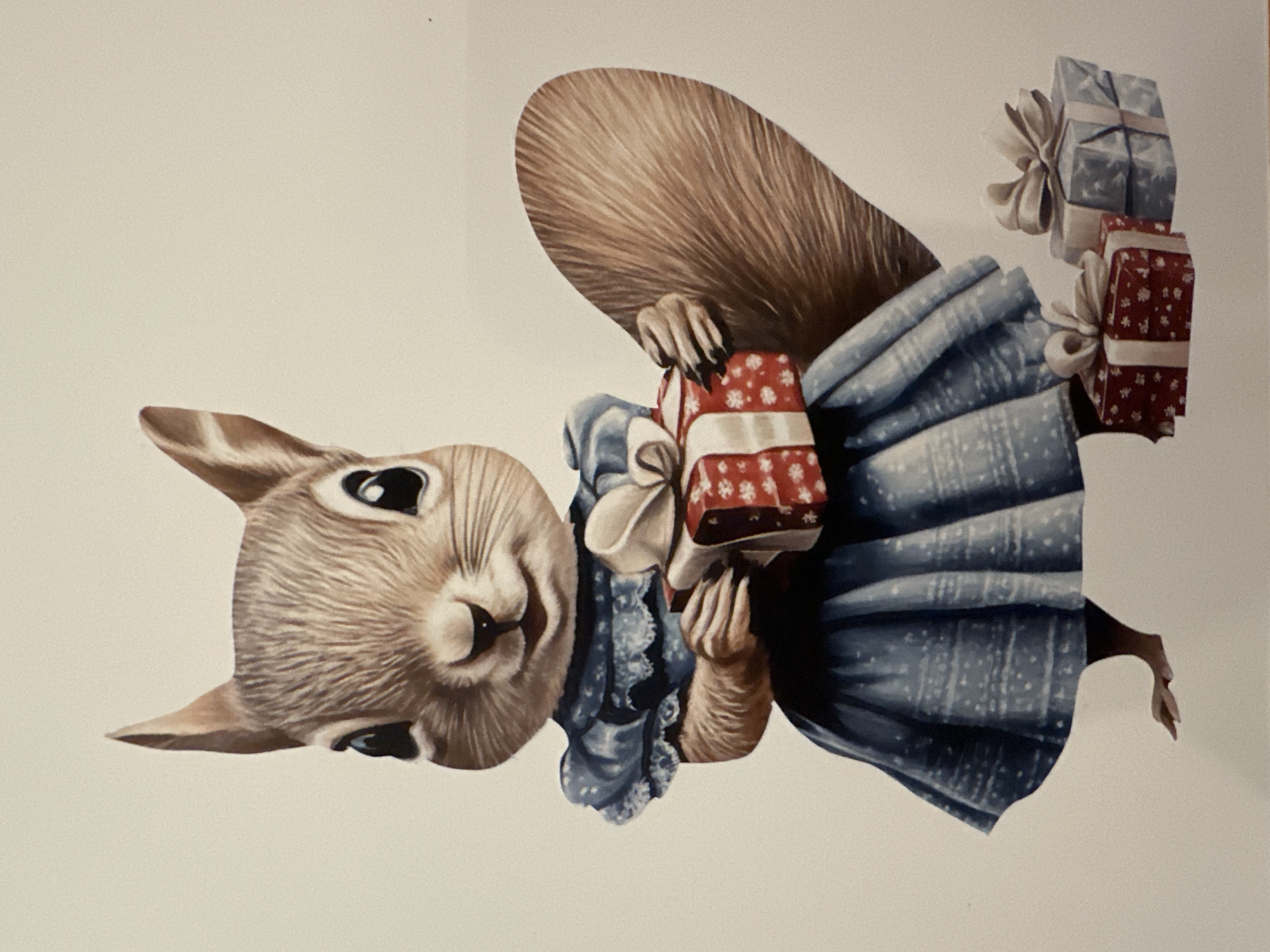A digitally illustrated image depicts a cartoon squirrel wearing a blue dress, holding a red and white wrapped gift. The squirrel has large, dark eyes, pointed ears, and a fluffy brown tail. The dress is detailed with lace trim and a patterned skirt. In the foreground, to the right of the squirrel, are two additional wrapped gifts: one red and white, and another blue and white. The background is a plain off-white color. There is no discernible location in the city of Minsk, Belarus.