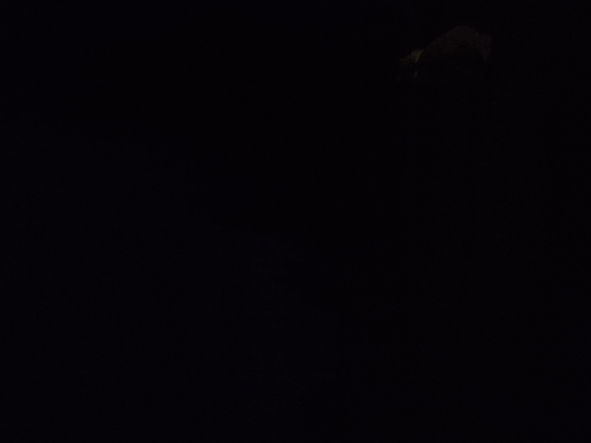The image is extremely dark, with the majority of it appearing completely black. In the lower right quadrant of the image, a faint, dimly lit object is visible. This object is roughly round or oval in shape and appears to be a small animal, possibly a rodent or a bird, with visible fur or feathers. The texture suggests it is sitting or crouching. The background is entirely black, indicating a dark environment or a poorly lit area. No specific location in Sooblase, Estonia can be identified from the visual information provided. There are no people, actions, or interactions depicted.