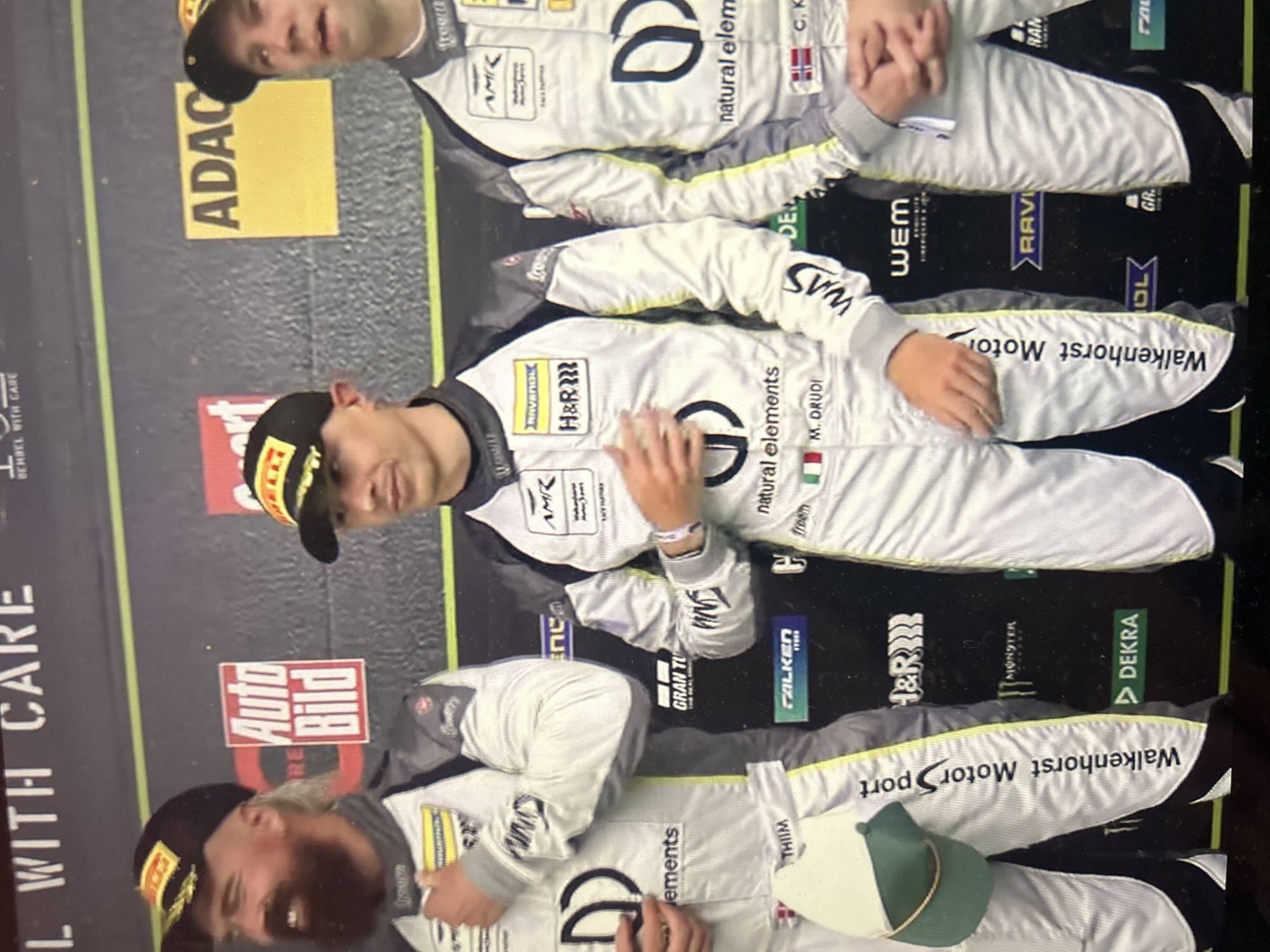Three men in racing suits stand on a podium. All three men wear caps. The man in the center wears a black and yellow cap. The podium has sponsor logos, including Walkenhorst Motorsport, H&R, Monster, DEKRA, ADAC, Auto Bild, and natural elements. There is no indication of this image being taken in Sofia, Bulgaria.