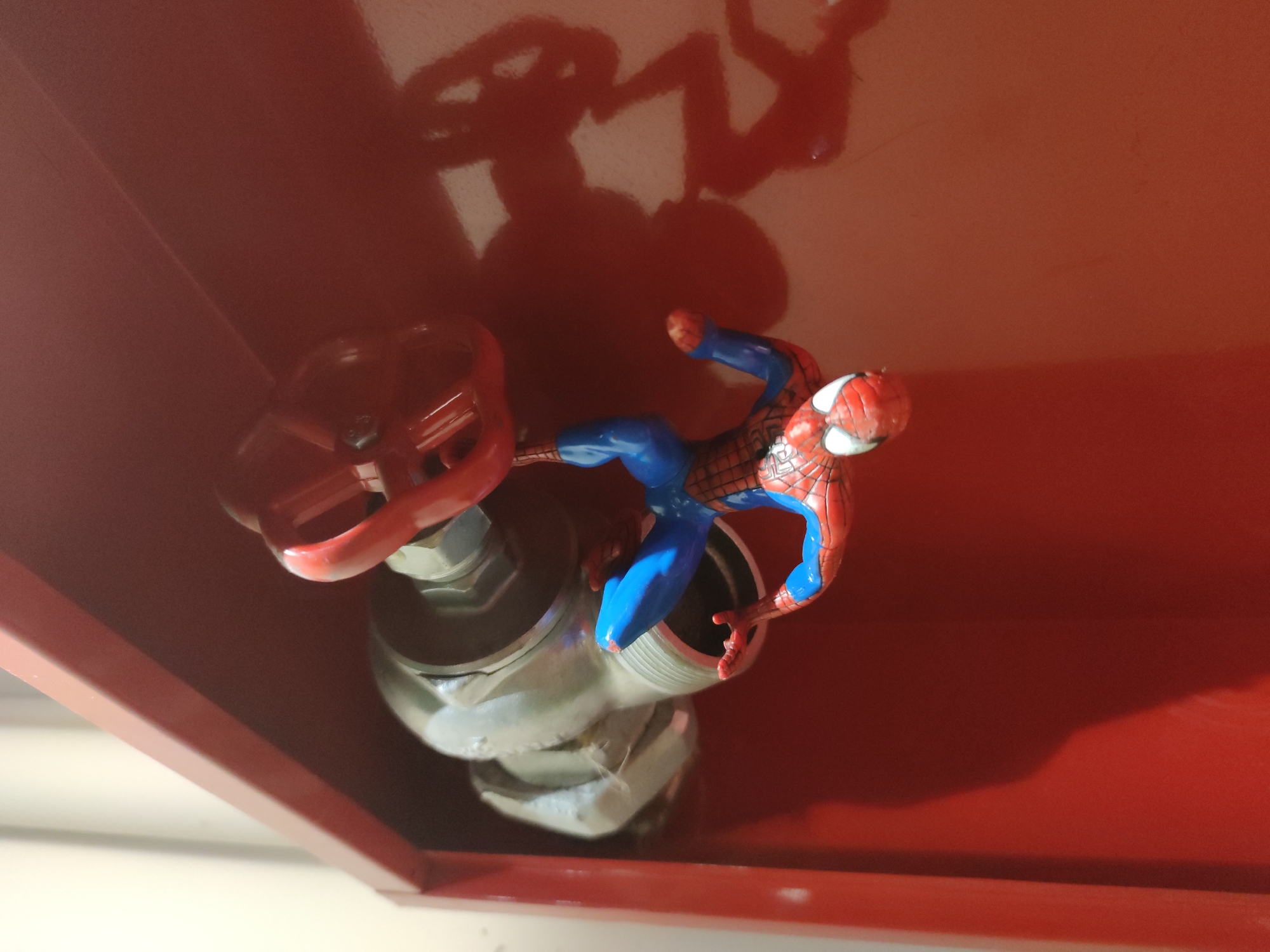 The image shows a Spiderman action figure perched on a red fire hydrant inside a red box. The hydrant has a large red valve wheel. The interior of the box is red. The location is unknown.