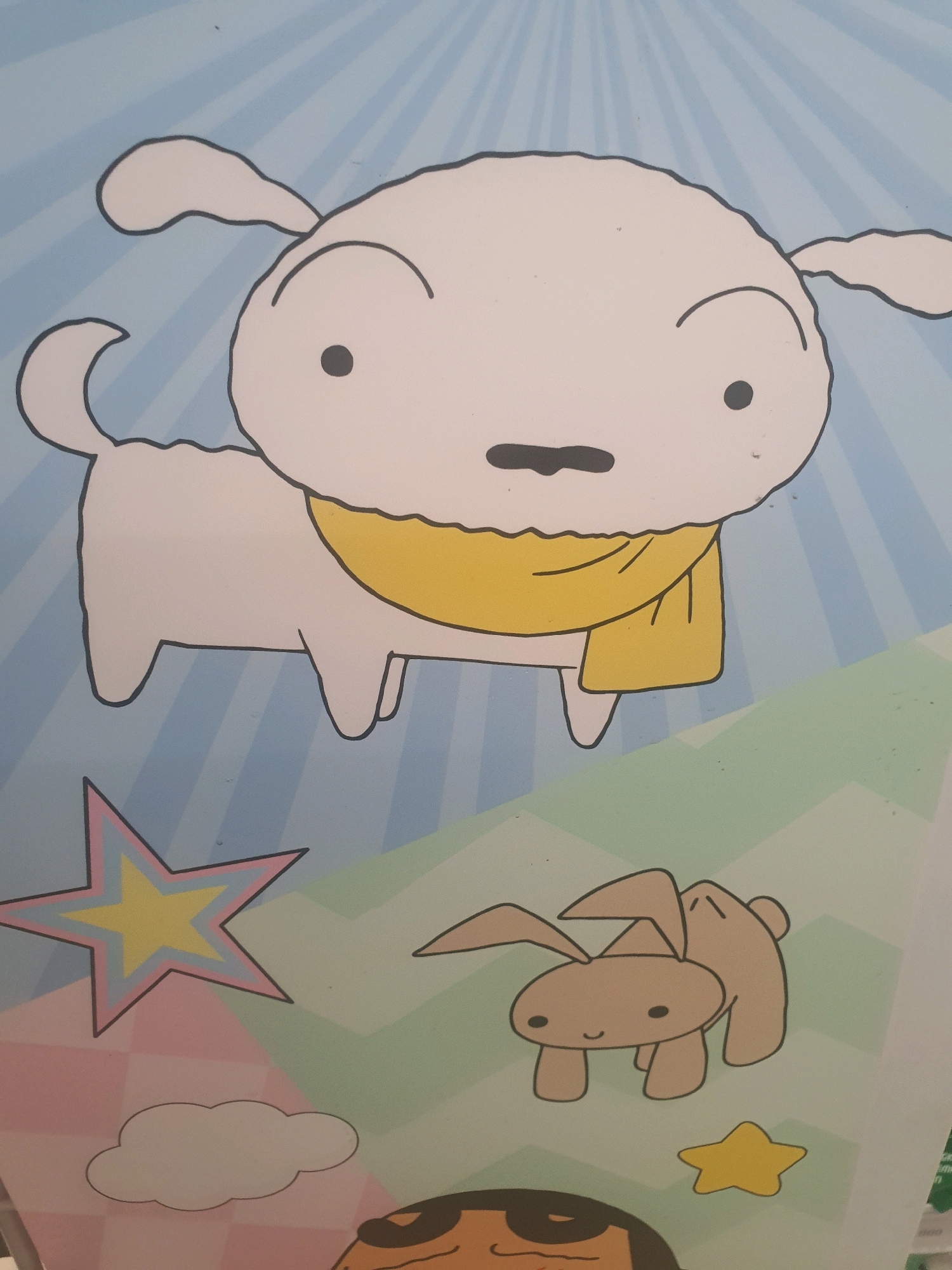 The image displays a cartoon drawing featuring a white dog with a yellow scarf, a tan rabbit with long ears, a yellow star with pink and blue outlines, a white cloud, and a partially visible cartoon face. The background is a light blue with radiating lines, transitioning to a pastel-colored checkered pattern with diagonal green and pink stripes. The style is simplistic and childlike. The image is a photograph of a poster or artwork.