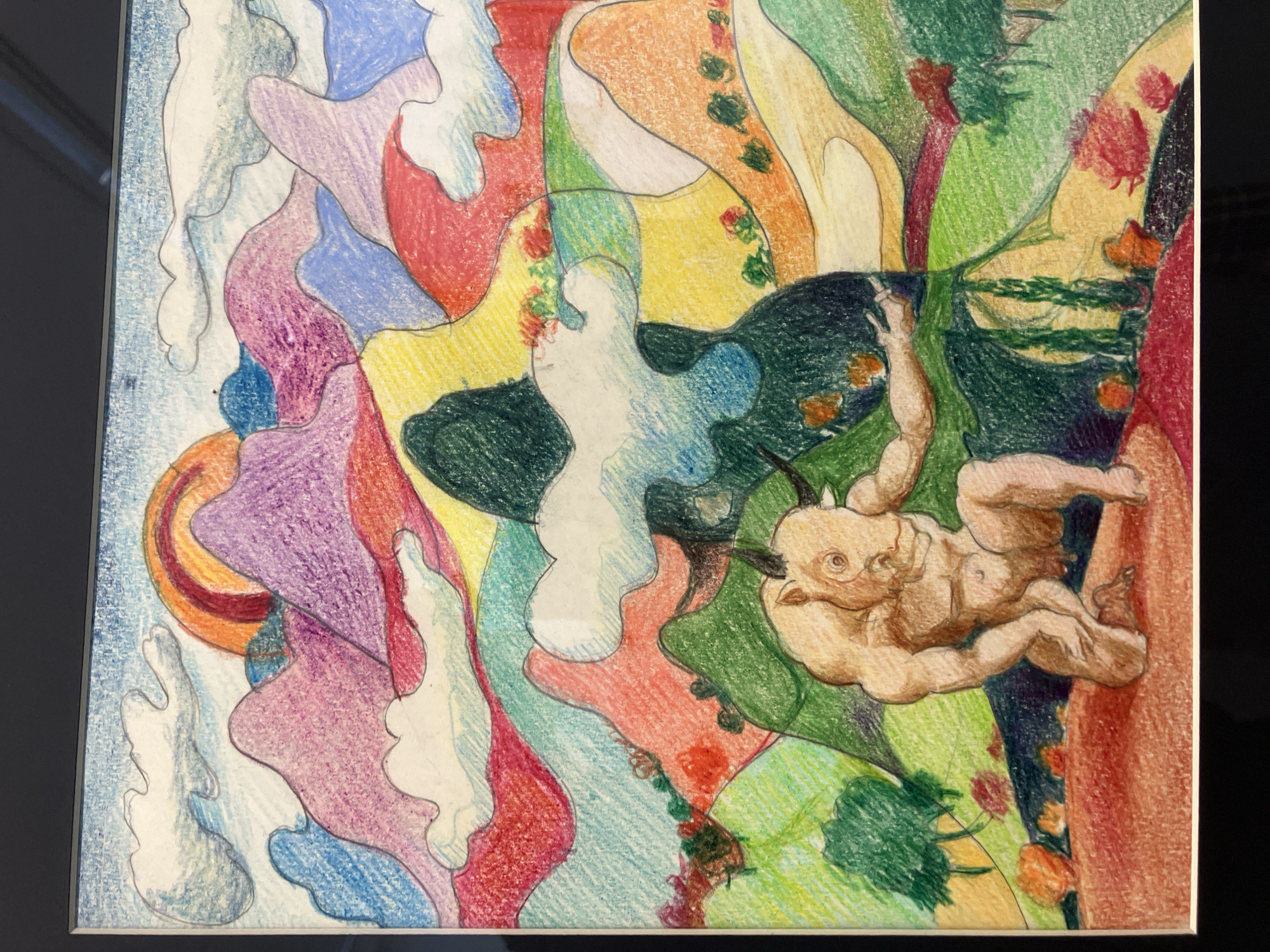 The image depicts a framed drawing or painting with an abstract composition of colorful shapes. Predominant colors include blues, purples, reds, yellows, and greens. A humanoid figure with horns is rendered in a more realistic style on the right side, grasping onto what appears to be a tree or foliage. The figure is a light skin tone and depicted in a dynamic, climbing pose. The background is abstract and colorful, reminiscent of a surreal landscape. The location (Tbilisi, Georgia) is not discernible within the image itself; there are no landmarks, signs, or visual elements that specifically indicate Tbilisi.