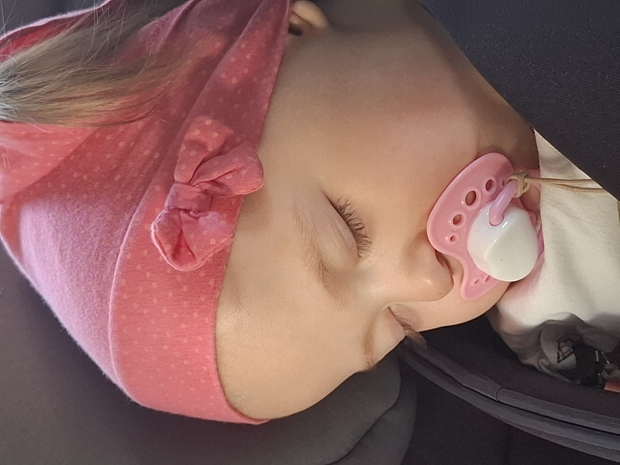 A child, likely a toddler, is shown asleep. The child is wearing a pink head covering with a bow. They have a pink pacifier in their mouth. The location and city of Chaikovsky, Russia are not discernable from the provided image.