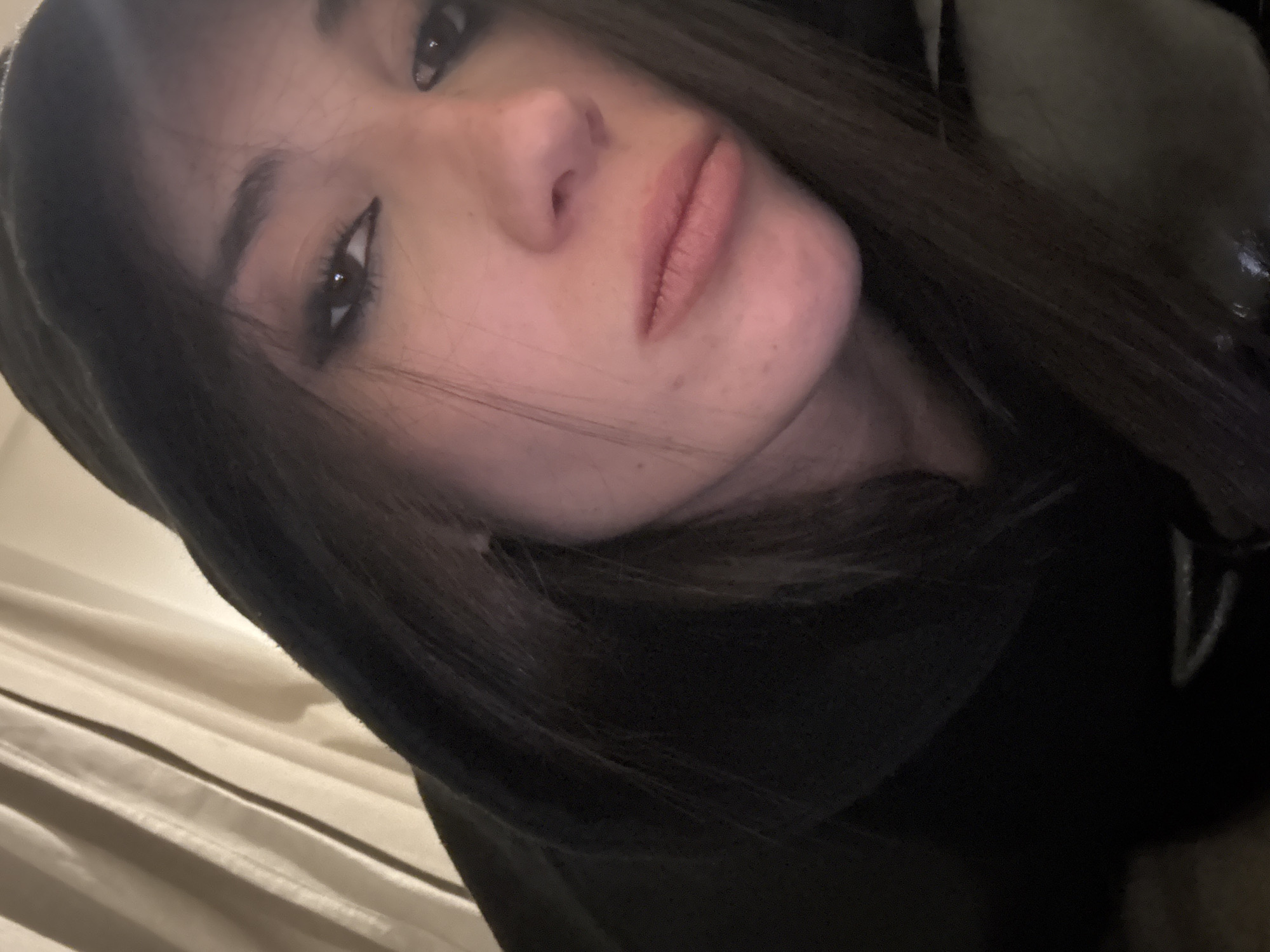A close-up selfie of a woman with fair skin and dark hair. She is wearing a dark hooded sweatshirt. The background is a light-colored, textured surface, possibly curtains or a wall.
There is no information in the image that supports a location in Buenos Aires, Argentina.