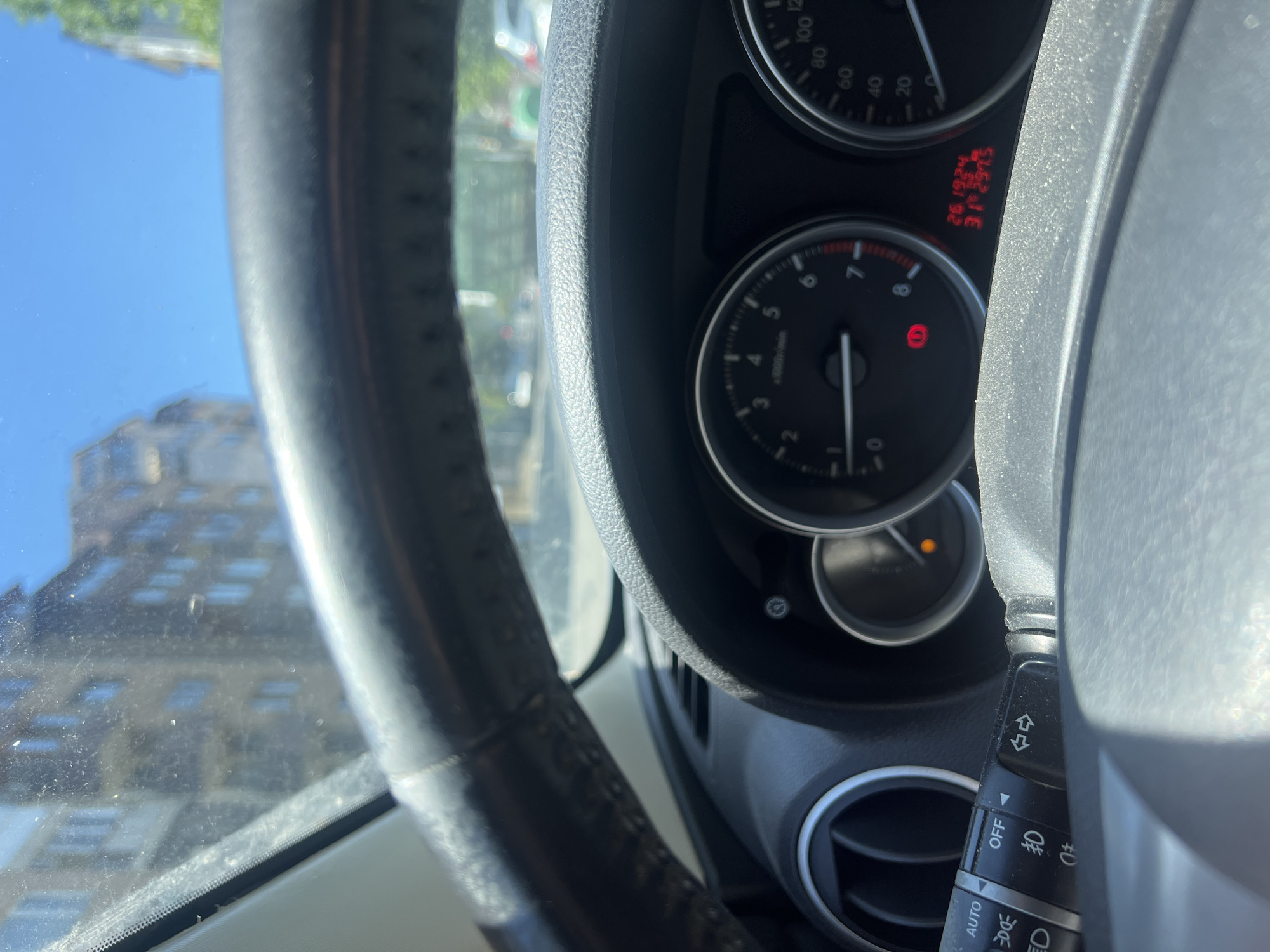 The image shows the dashboard of a car. The speedometer and tachometer are visible. The tachometer indicates an engine speed around 1000 RPM. The odometer reading is 26,1924. The gear shift lever is visible on the right side of the frame. Through the windshield, there is a building. The location cannot be definitively determined as Burgas, Bulgaria based on the image content.