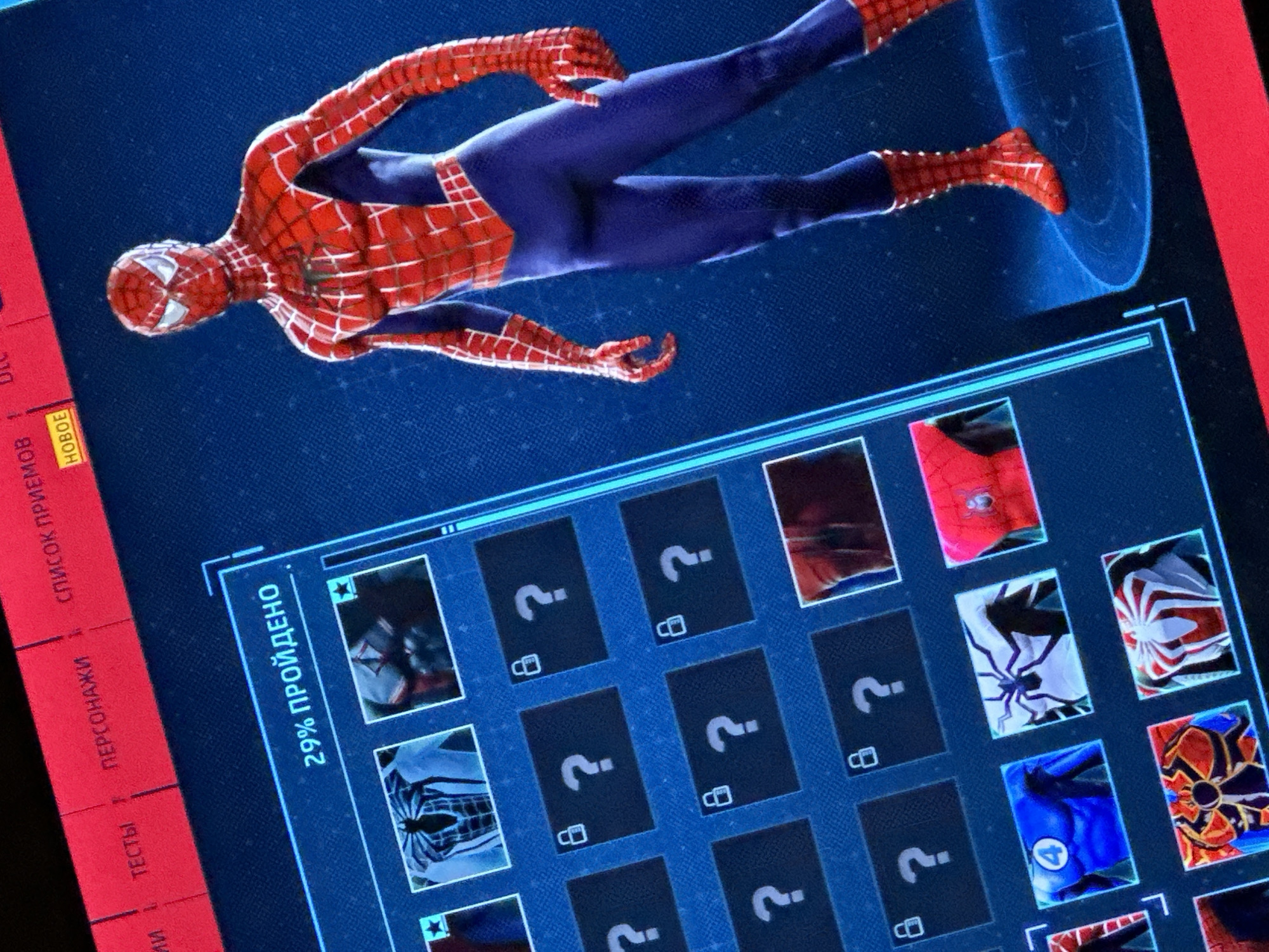 A screen displays a Spider-Man character selection menu from a video game, positioned at an oblique angle. Spider-Man, in his classic red and blue costume, is displayed above the menu as if hovering. The character selection screen shows various suits, some of which are unlocked and visible while others are still locked, indicated by question marks and lock symbols. The progress bar at the top indicates that 29% of the game has been completed. Menu options in Russian are visible on the left side of the screen: "TECTbl," "ПЕРСОНАЖИ," and "СПИСОК ПРИЕMОВ," with "HOBOE" (New) highlighted.