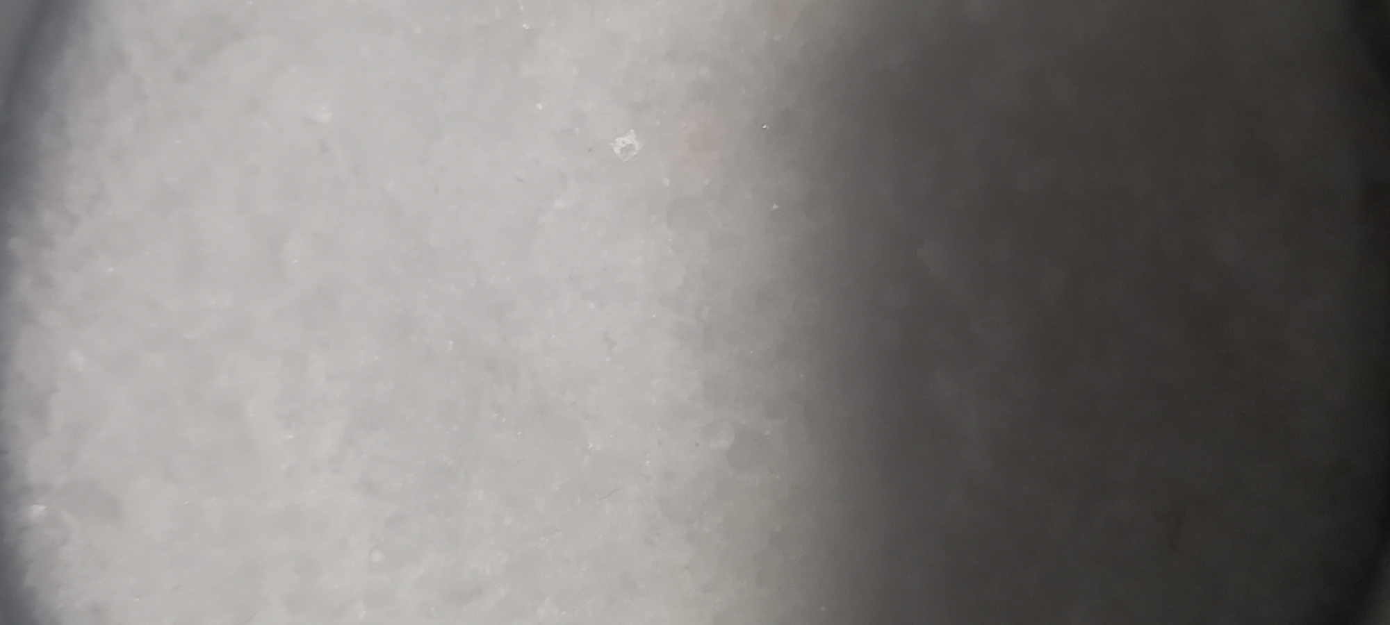 The image shows a close-up, slightly out-of-focus view of a white, granular surface. There are variations in texture and tone across the image. The left side appears brighter and more textured, while the right side is darker and smoother, potentially due to shadows. The composition is abstract and lacks identifiable objects. The image cannot be associated to the city of Kryvyi Rih, Ukraine.