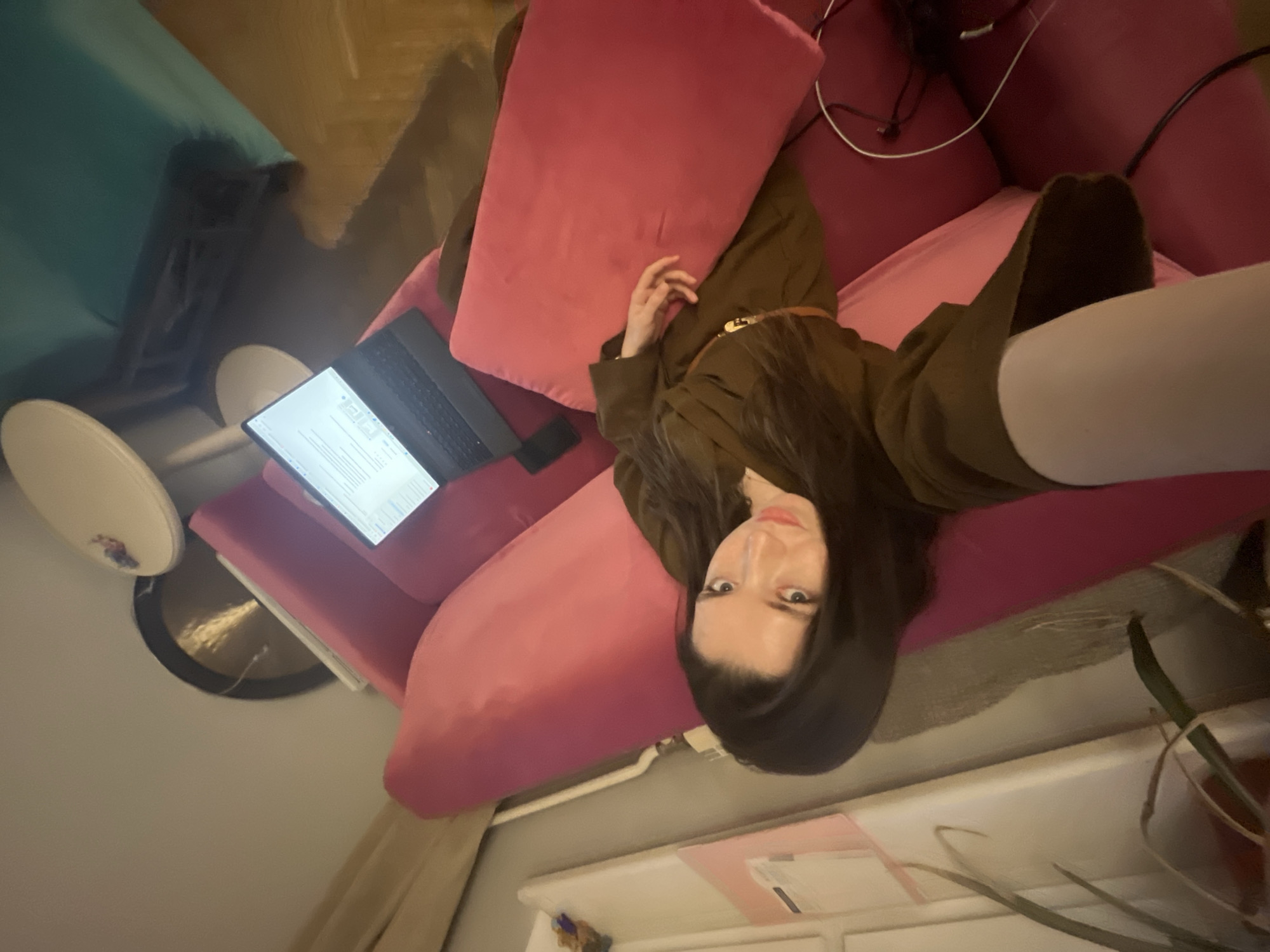 A woman lies on a pink sofa, using a laptop. The scene also includes furniture such as chairs, tables, and cabinets. A gong is visible on the floor. The precise location is undetermined; Moscow, Russia is unconfirmed.