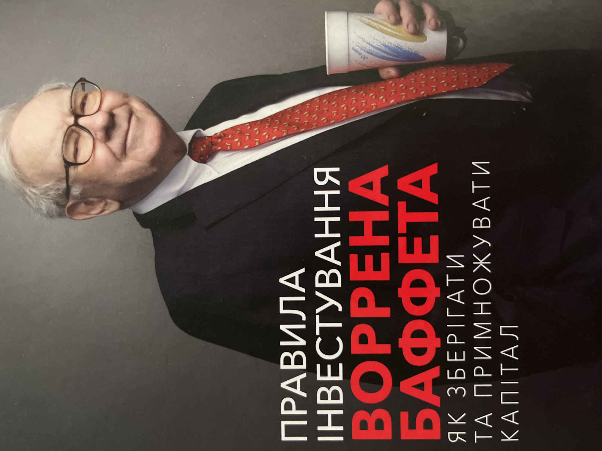 This image shows a book cover with a picture of Warren Buffett in a suit and tie, holding a disposable cup. The text on the cover is in Ukrainian, with "ВОРРЕНА БАФФЕТА" prominently displayed in red. Given the text is in Ukrainian, it is reasonable to assume that the book may be found in Kryvyi Rih, Ukraine, among other places where Ukrainian is spoken.
