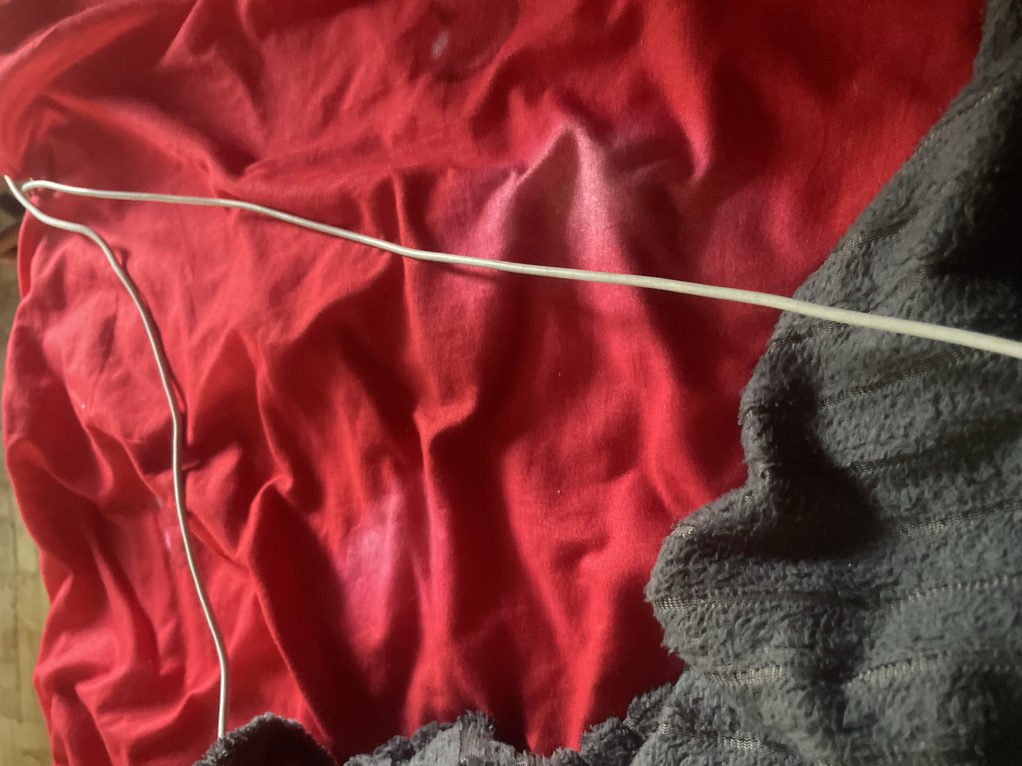 A light-colored cable is visible on a red, wrinkled fabric surface, partially obscured by a dark, textured fabric on the left side of the image. The scene is indoors and appears to be on a bed or similar surface, given the textures of the fabrics. No specific location in the city of Линёвка, Russia, can be determined from the visual information provided.