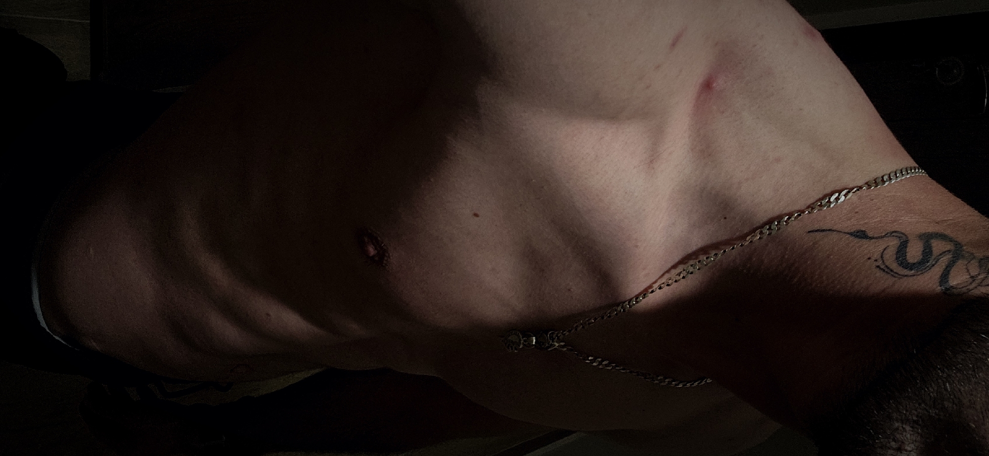 A close-up photograph shows a torso with a silver chain necklace. A tattoo is visible on the upper arm. The location of the photograph is not discernible. The image contains no information indicating the scene is in Plovdiv, Bulgaria.