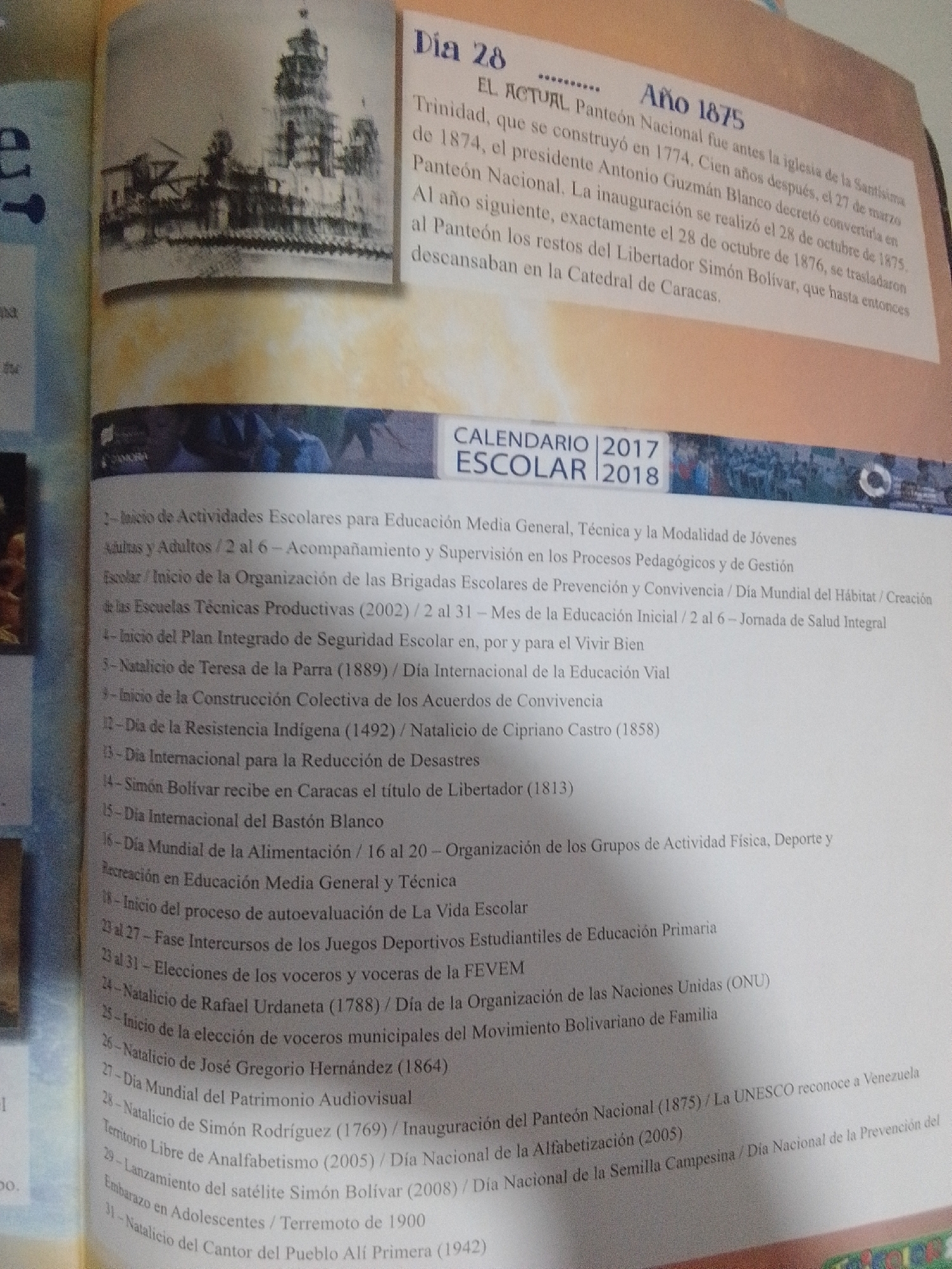 The image shows a page from a book with two distinct sections. The top section features a black and white historical photograph of a large, multi-tiered building resembling a cathedral or monument, with scaffolding visible to its left, suggesting ongoing construction or renovation. To the right of the photograph is text in Spanish detailing an event on "Dia 28" and "Año 1875" concerning the Pantéon Nacional in Trinidad, mentioning its inauguration and the transfer of Simón Bolívar's remains.
The bottom section of the image contains a list of dated events in Spanish, presented as a calendar. The heading "CALENDARIO 2017 2018" is visible. The numbered list includes entries such as "Inicio de Actividades Escolares," "Natalicio de Teresa de la Parra," "Día de la Resistencia Indígena," "Simón Bolívar recibe en Caracas el título de Libertador," and "Elecciones de los voceros y voceras de la FEVE." The text is predominantly black on a white background.
There is no information within the image that places any part of it in the city of La Tagua, Venezuela.