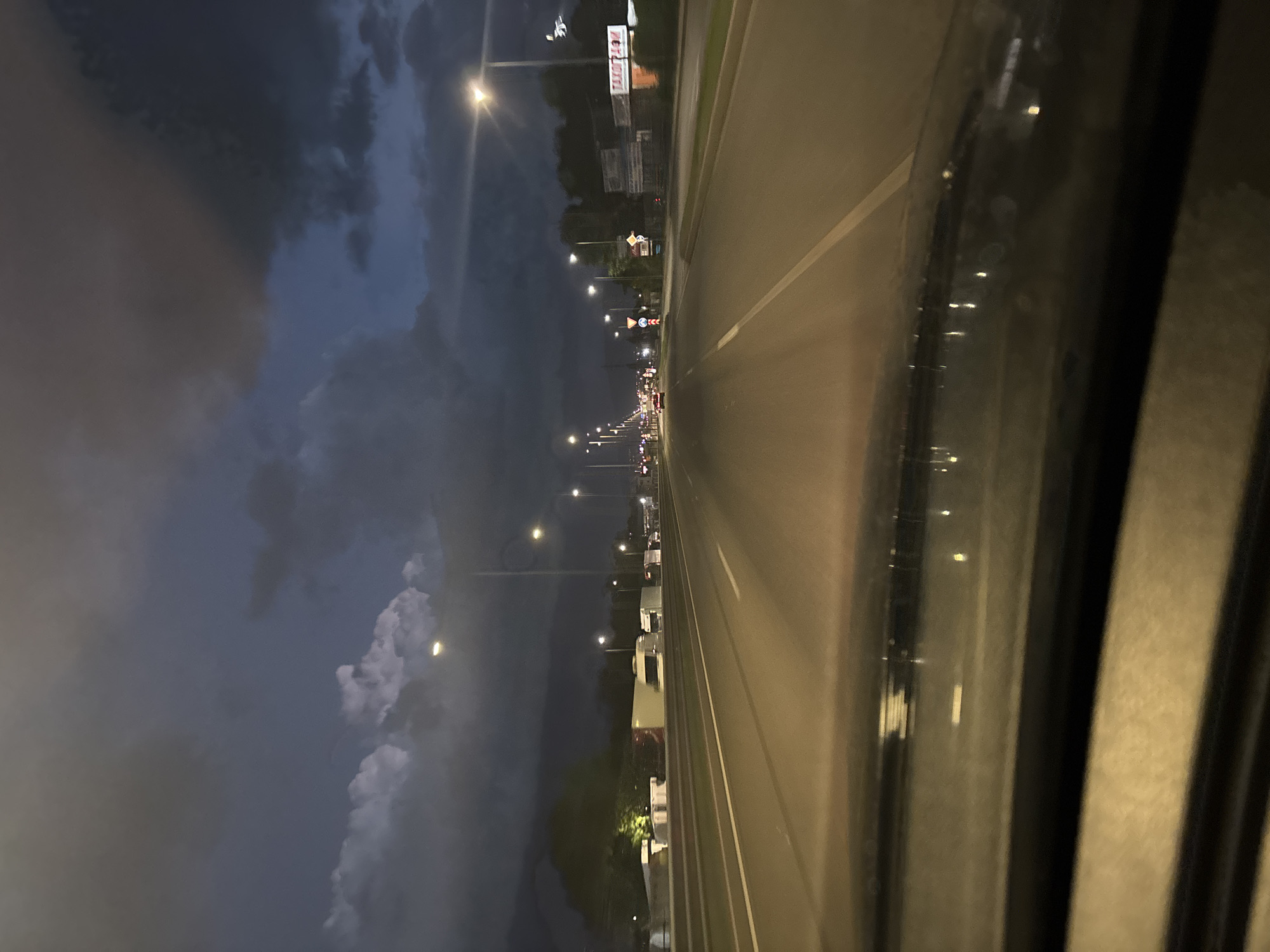 The image depicts a nighttime view of a road, likely taken from inside a vehicle. The road is illuminated by streetlights, and there are other vehicles visible in the distance. Dark, stormy clouds fill the sky to the left of the road. The foreground shows the interior of the vehicle, possibly the driver's side window.
Without further details or context, it's impossible to identify the exact location in Sofia, Bulgaria.