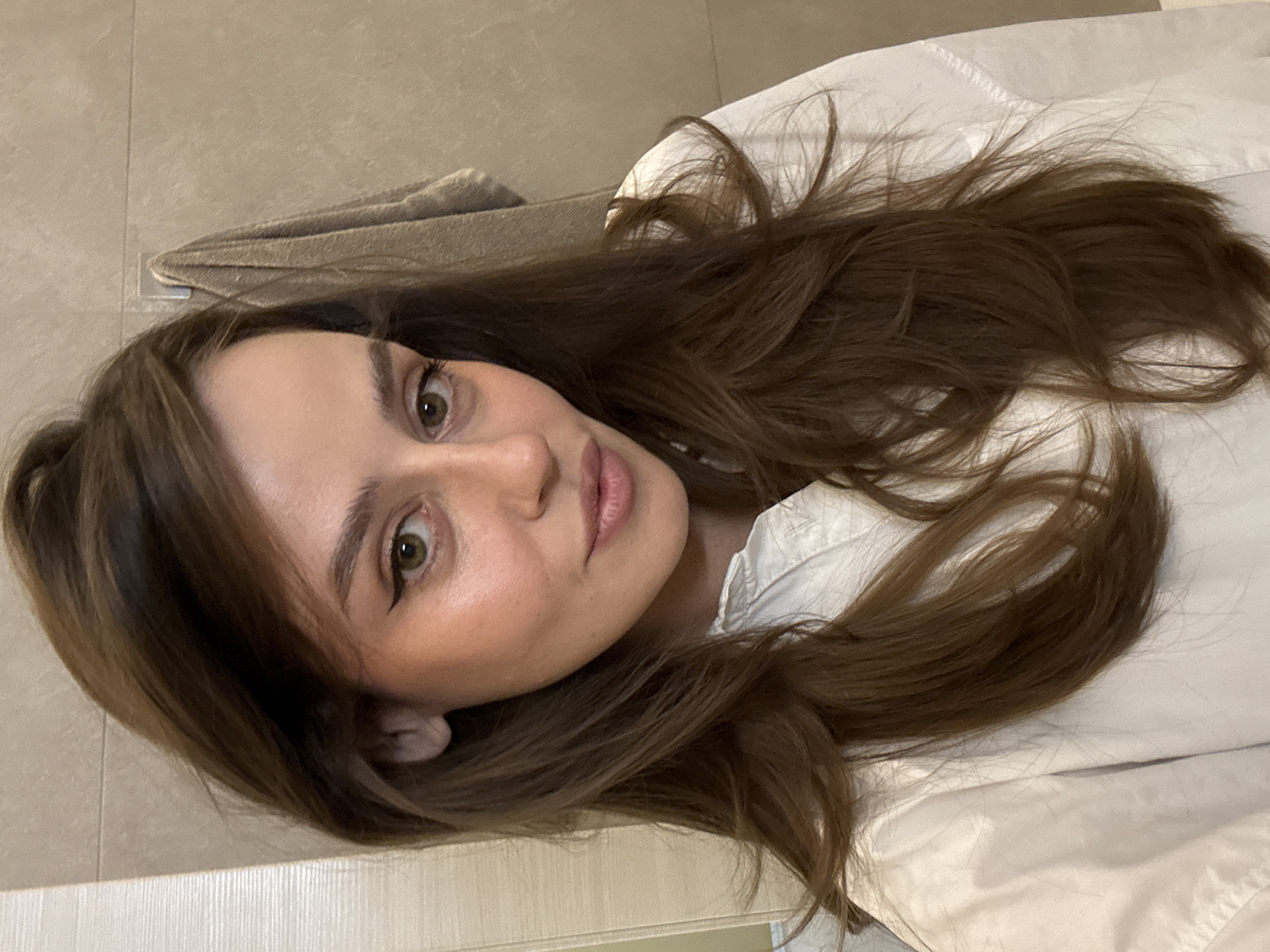 A young woman with long brown hair is lying on what appears to be a white surface. The location seems to be a bathroom or a room with tiled walls and a towel hanging in the background. The photograph does not provide sufficient information to determine any specific location in Krasnoyarsk, Russia.