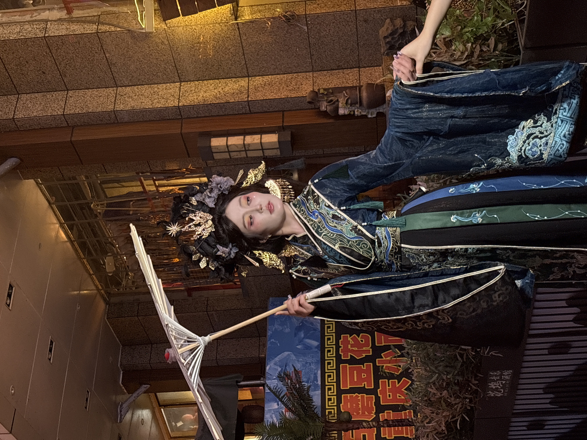 A woman in traditional Chinese attire stands outdoors in the Yuzhong District of China. She is holding a decorative parasol. The background includes building facades and promotional signs written in Chinese characters.