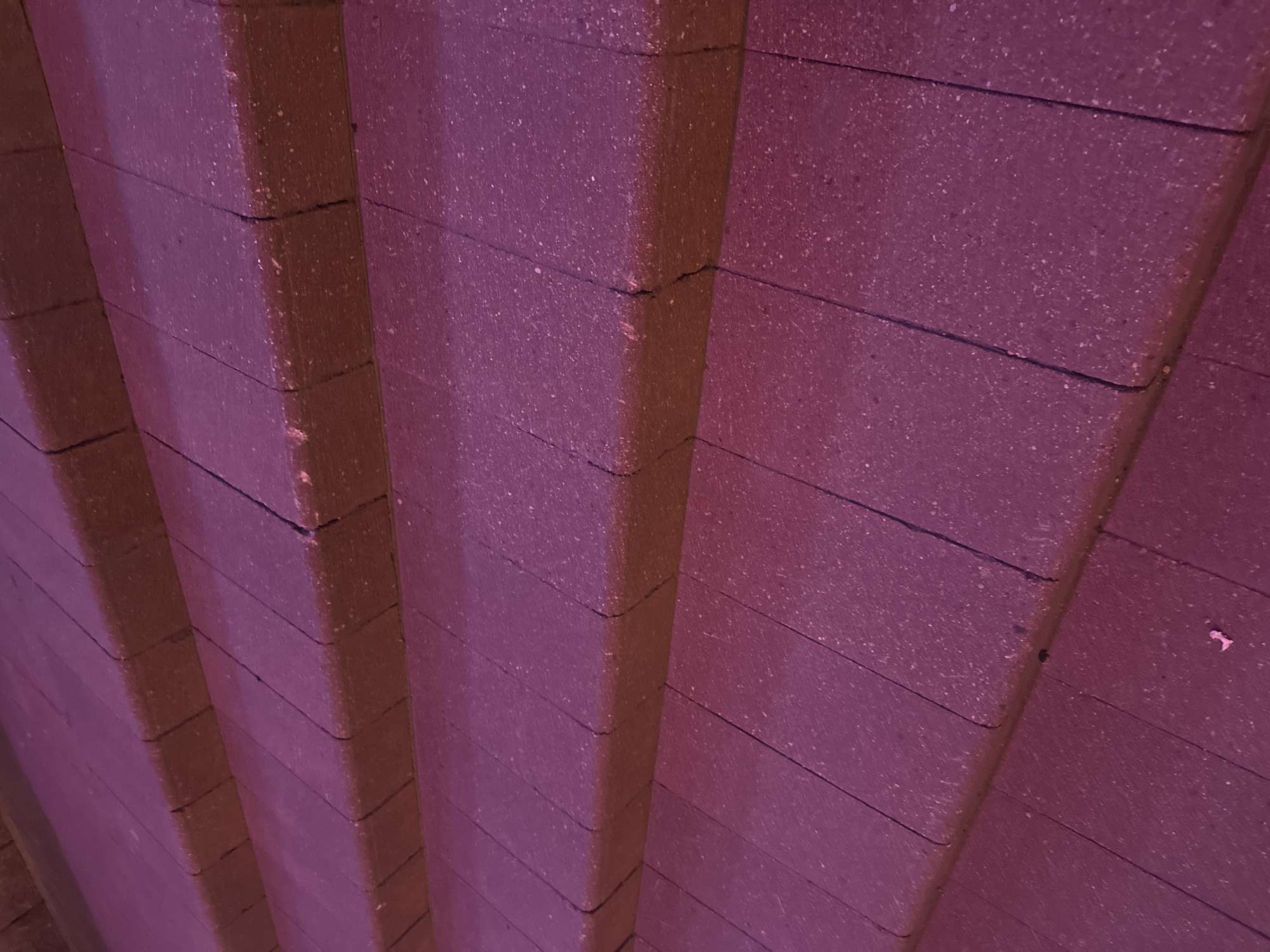 The image displays a close-up, angled view of several steps made of reddish-purple, speckled stone or concrete. The steps are arranged in a diagonal pattern, leading upwards from the bottom left to the top right of the frame. Each step is comprised of multiple rectangular pavers, with visible grout lines separating them. The surface of the steps appears textured. The lighting casts a deep magenta hue over the entire scene, obscuring fine details and suggesting artificial lighting or a specific time of day. There are no people, animals, or distinct landmarks visible in the image. The scene depicts an outdoor architectural feature, likely part of a staircase or walkway. The location is identified as Minsk, Belarus, though no specific geographical markers are present in the visual content.