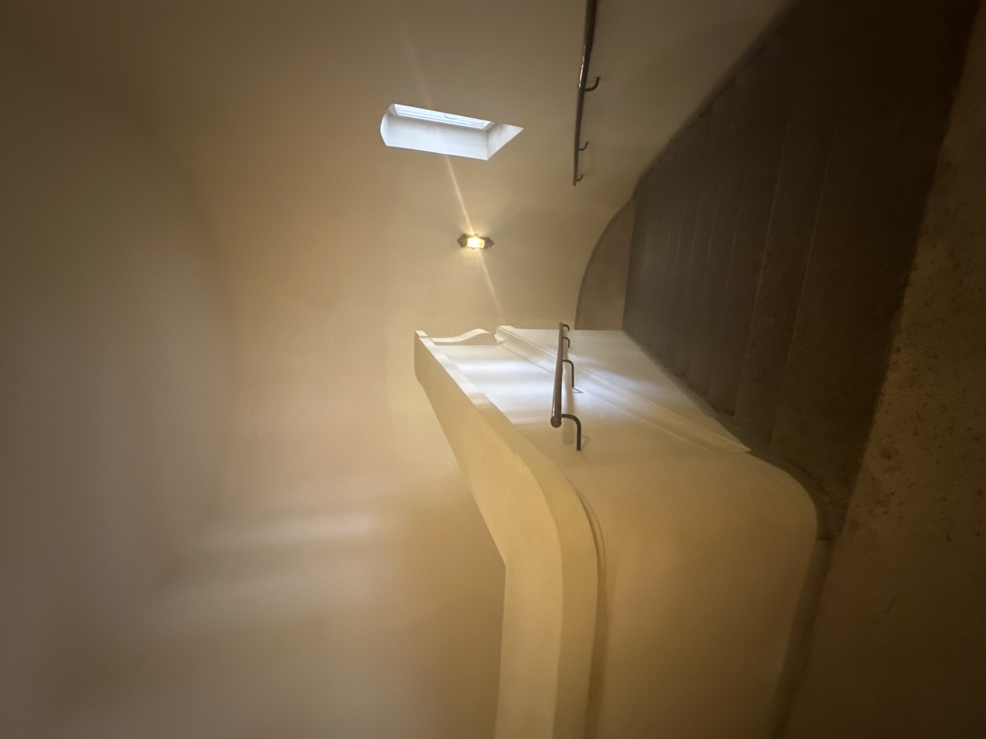 This media file depicts a curved staircase in a building, likely an interior space. The staircase is made of a smooth, light-colored material, possibly concrete or plaster, and features a sleek, modern design. A handrail runs along the outer edge of the staircase, made of dark metal. Above the staircase, a skylight is visible in the ceiling, admitting natural light. A light fixture is also present on the ceiling, casting a warm glow. The walls surrounding the staircase are painted a light, neutral color, and there appears to be a darker, textured wall on the right side of the image. The scene is dimly lit, with the natural light from the skylight and the artificial light from the fixture creating areas of light and shadow. The overall impression is one of a clean, contemporary architectural space, possibly a residential building, a hotel, or a public institution. There is no activity or event taking place; the image is a static depiction of the staircase and its surroundings. No people are visible. The time of day cannot be determined definitively, but the presence of natural light suggests it is daytime. There are no weather cues. The location context provided is Odesa, Ukraine, but there are no specific visual cues in the image to confirm this. No text is visible in the image.