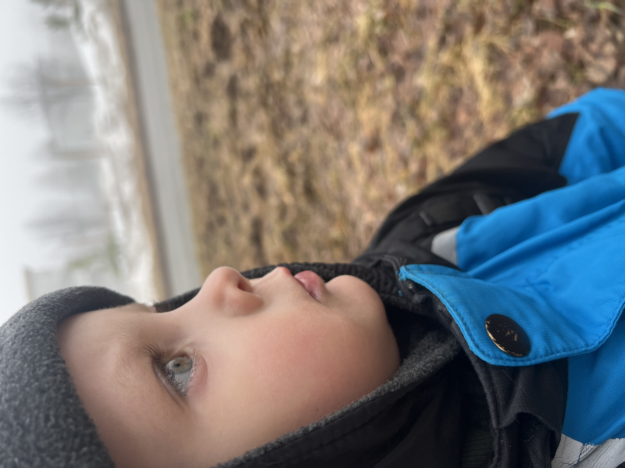 A child in a grey beanie and blue jacket lies on the ground. A road and field appear in the background. The location is Markovskiy, Russia.