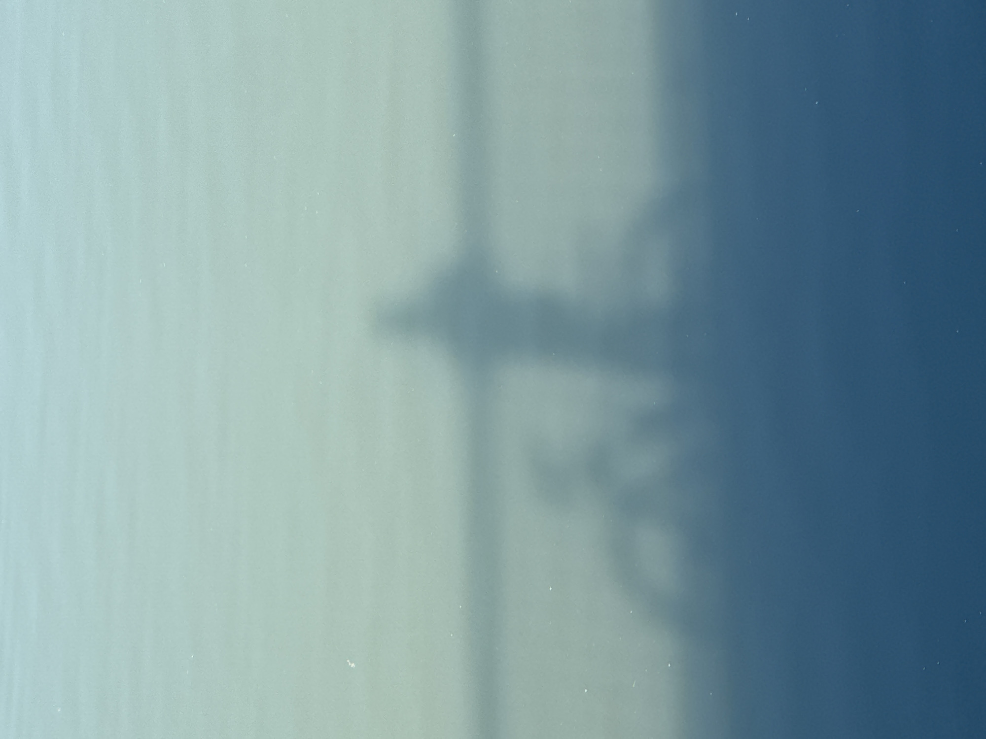 The image shows a blurred silhouette of a person standing on a bicycle reflected on a body of water. The water is a gradient of light blue and green, with darker blue at the bottom. The reflection is distorted by the ripples on the water's surface. The scene appears to be outdoors, possibly on a lake or river in Rostov-on-Don, Russia, given the color and nature of the water. The silhouette of the person is upright, with arms outstretched, while the bicycle is positioned in front of them. The overall impression is one of a serene and tranquil moment captured in a somewhat abstract manner due to the reflections.