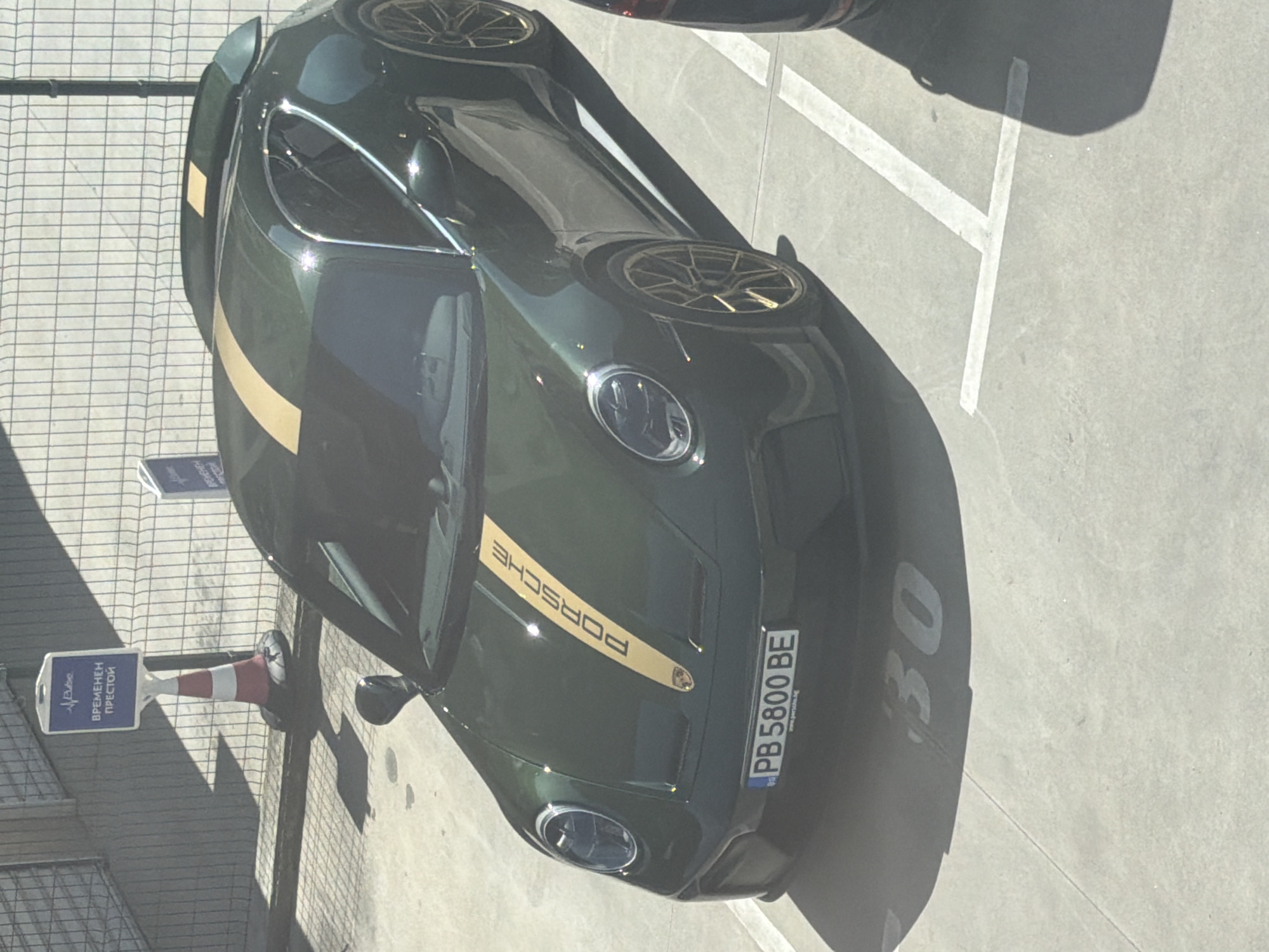 The image shows a dark green Porsche 911 GT3 with a gold stripe parked in a parking lot. The car has the number "30" displayed on the hood. The license plate reads "PB 5800 BE." A traffic cone with a sign that reads "ВРЕМЕНЕН ПРЕСТОЙ" (Temporary Stay) in Bulgarian is visible in the lower left corner. The location appears to be outdoors. While the exact location is not definitively determined by the image, it is in Bulgaria.