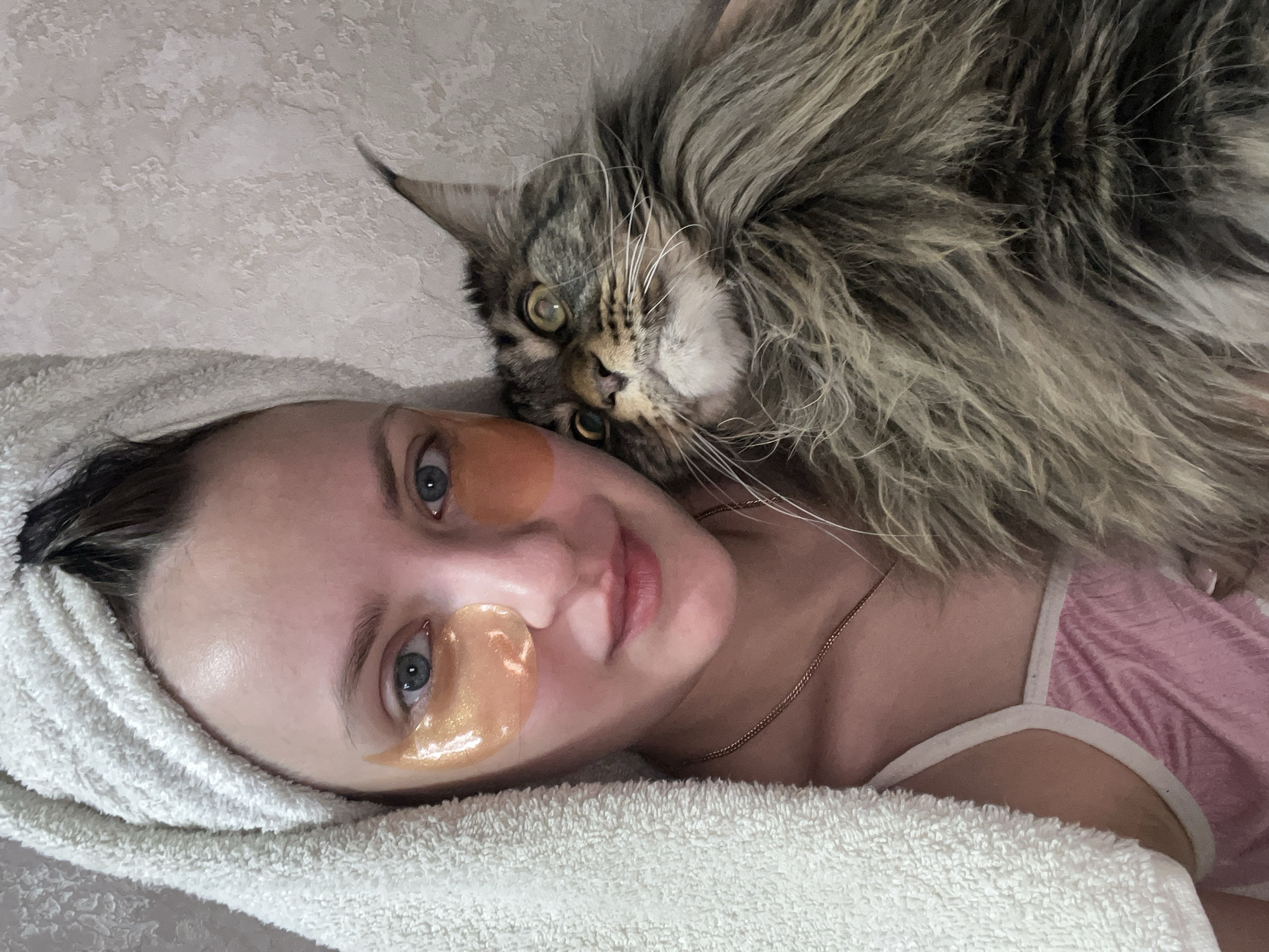 A woman wearing eye masks and a towel is lying down next to a large, long-haired cat. The location is Марковский, Russia.