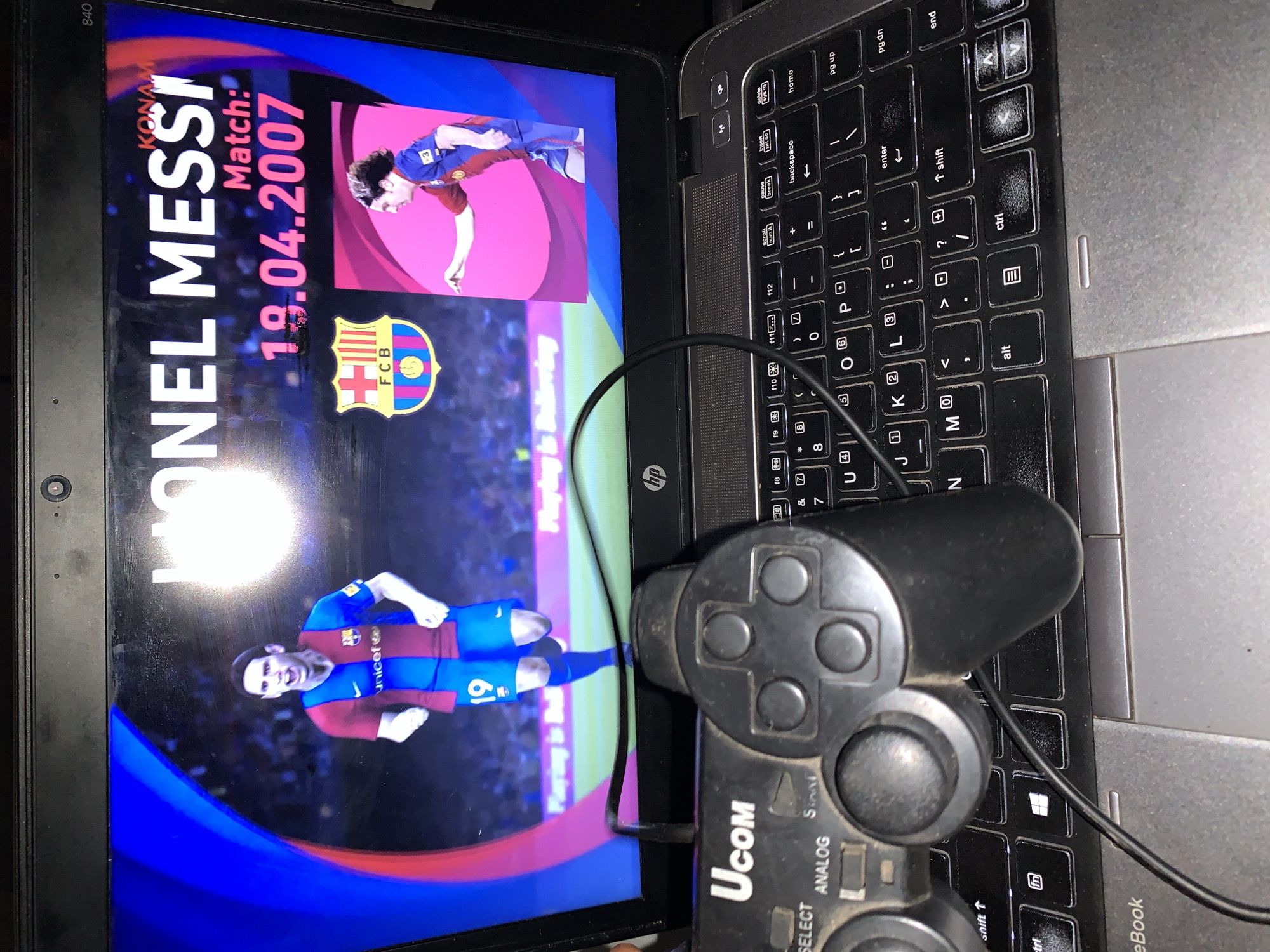 The image shows a laptop displaying a Konami football game featuring Lionel Messi. The screen shows "Lionel Messi Match: 19.04.2007" and the FCB Barcelona logo. A UCOM brand gamepad is resting on the keyboard. The laptop model is likely an HP 840. The scene does not have any discernible location that indicates Rafin Par, Nigeria.