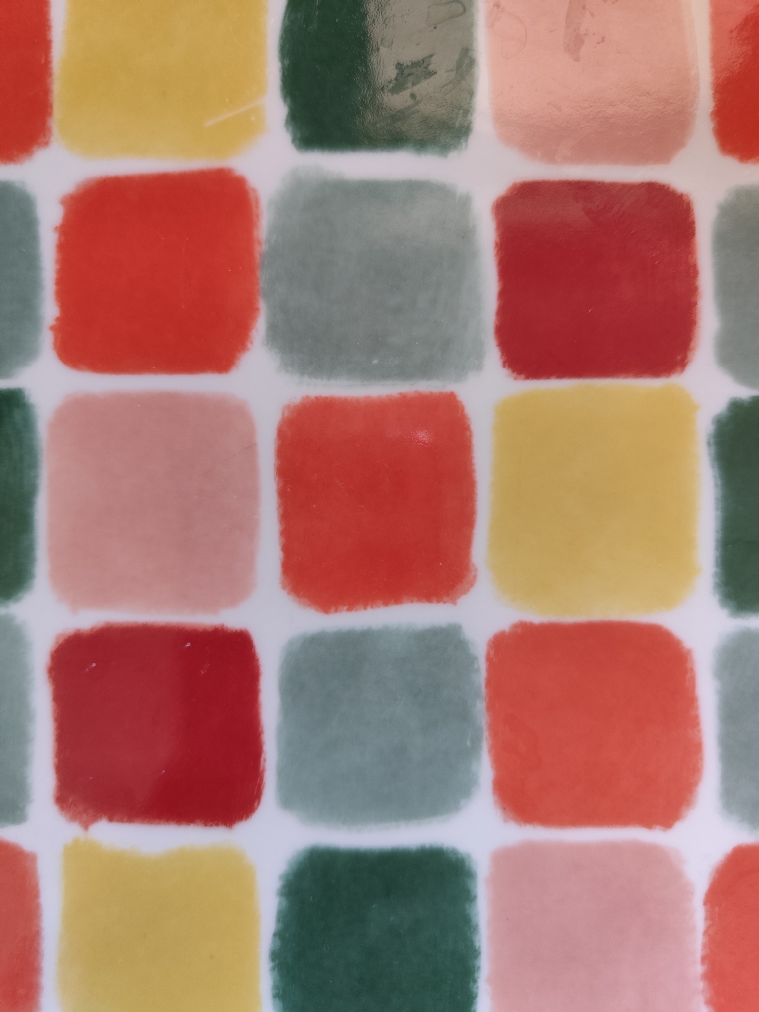 The image shows a close-up of a pattern consisting of squares of various colors (red, yellow, green, pink, and gray) separated by white lines. The image does not contain any information to determine its location in the city of Giarre, Italy. The pattern appears to be on a flat surface, possibly a tile or a tabletop. The colors are somewhat muted and the overall appearance is slightly glossy.
