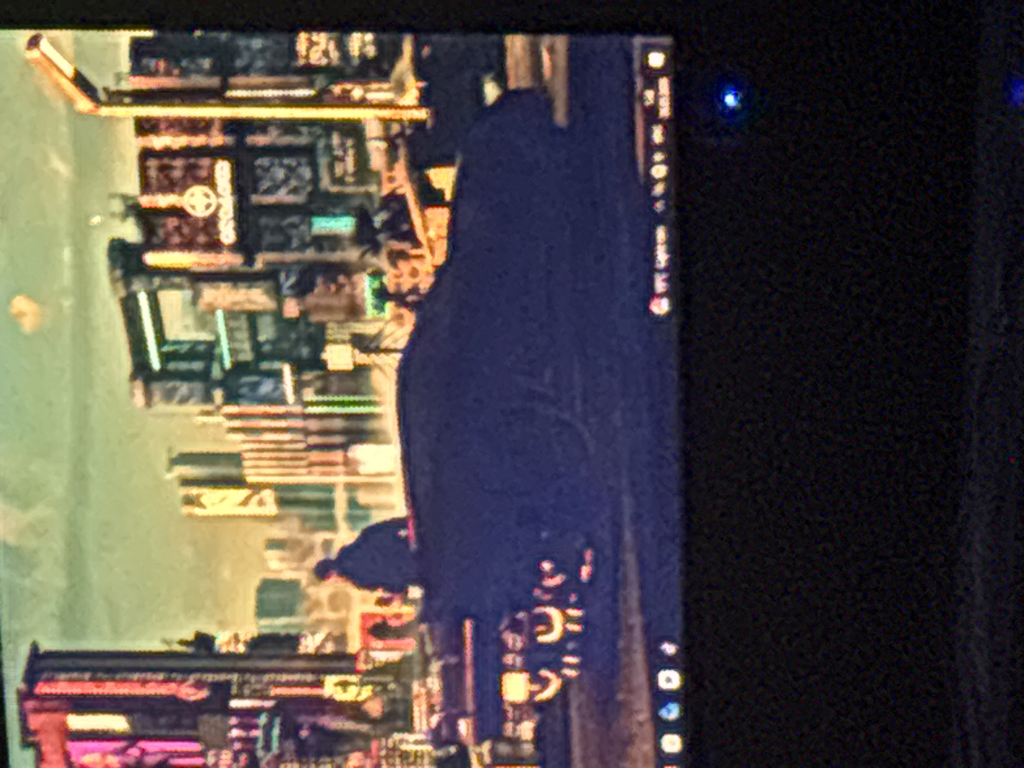 The image shows a monitor screen displaying a wallpaper or background featuring a cityscape with an urban, possibly futuristic, design. The lower right corner of the screen displays the taskbar with application icons. There's a dark, blurry form, possibly a person or object, obscuring part of the cityscape in the center. The surrounding environment is dark, and there appears to be a faint blue light in the upper right corner, likely from an electronic device. No specific details suggest a location in Yerevan, Armenia.