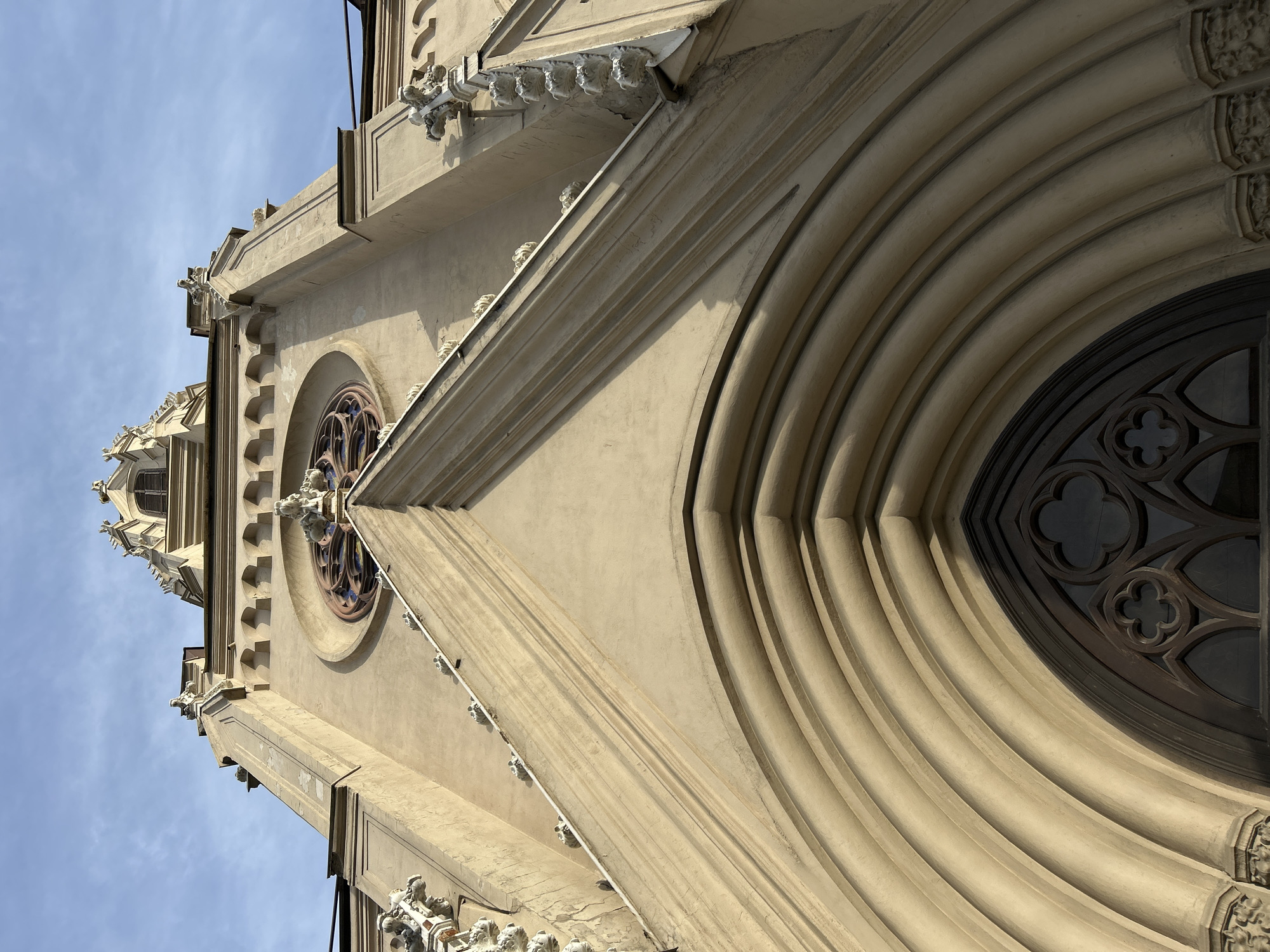 The image depicts an upward view of a building in Saint Petersburg, Russia. The building features Gothic architectural elements, including an arched entrance with ribbed moldings and a circular window with decorative tracery. Gargoyles and other ornamental details adorn the facade. The sky is partially visible in the background.