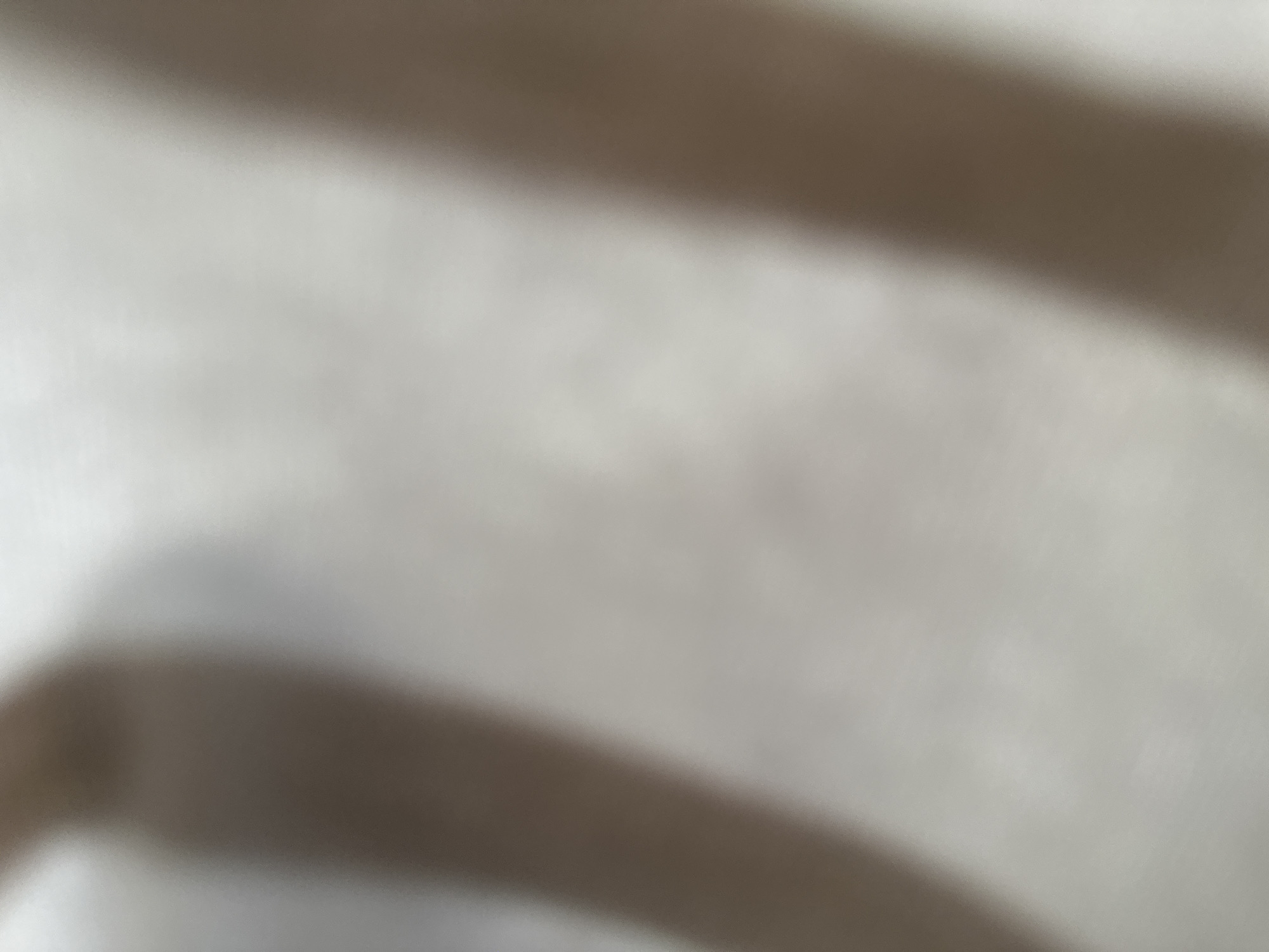 This is a highly blurred, abstract image, making it difficult to definitively identify subjects, objects, or a specific scene. The dominant feature is a gradient of light and shadow. A darker, diagonal band runs across the image from the top left to the bottom right, obscuring any details beneath it. The rest of the image is a lighter, uniform shade, suggesting a plain background or surface. There are no discernible people, objects, or activities. The lighting appears soft, but without clear context, it's impossible to determine the time of day or weather. No text is visible. Given the location context of Belgrade, Serbia, there are no visual cues to confirm or suggest this location. The overall impression is one of a soft, out-of-focus texture or light pattern.