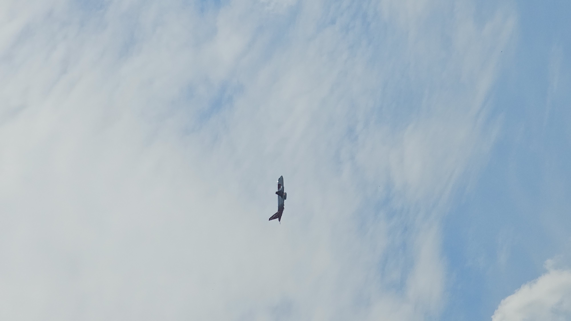 The image shows an airplane flying in a cloudy sky. The airplane is a passenger jet with a red and white livery. It is captured in mid-flight, with its wings spread and its engines visible. The sky is partly cloudy, with streaks of white clouds against a light blue background. The overall impression is one of a clear day with some cloud cover, typical for Yekaterinburg, Russia, a city known for its variable weather. The airplane's position in the sky suggests it is either taking off or landing, or cruising at a moderate altitude. The scene is devoid of any human presence on the ground, focusing solely on the aerial view of the aircraft.