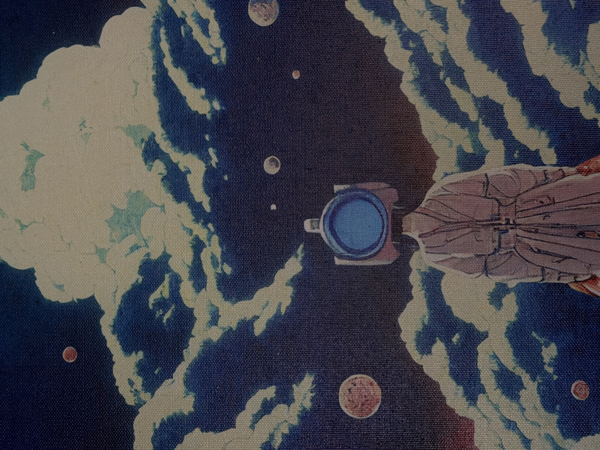 The image depicts a stylized, illustrative scene with a dark blue background suggesting a night sky or outer space, populated by numerous planets and swirling clouds in shades of white, yellow, and blue. In the foreground, a figure stands with their back to the viewer. This figure wears a light pink, long coat with intricate detailing and what appears to be a camera or a similar device as a head, featuring a large blue circular lens. The figure's pose suggests observation or contemplation. The overall aesthetic is dreamlike and surreal, with no identifiable connection to Naberezhnye Chelny, Russia.
