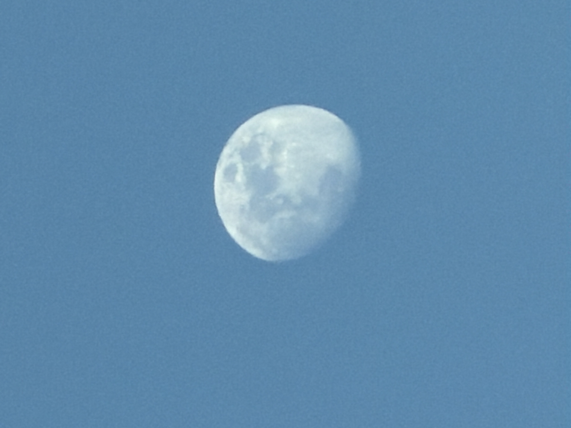 The image shows a waxing gibbous moon in a light blue sky. There are no people or other objects visible. There is no indication of the location being Moscow, Russia.