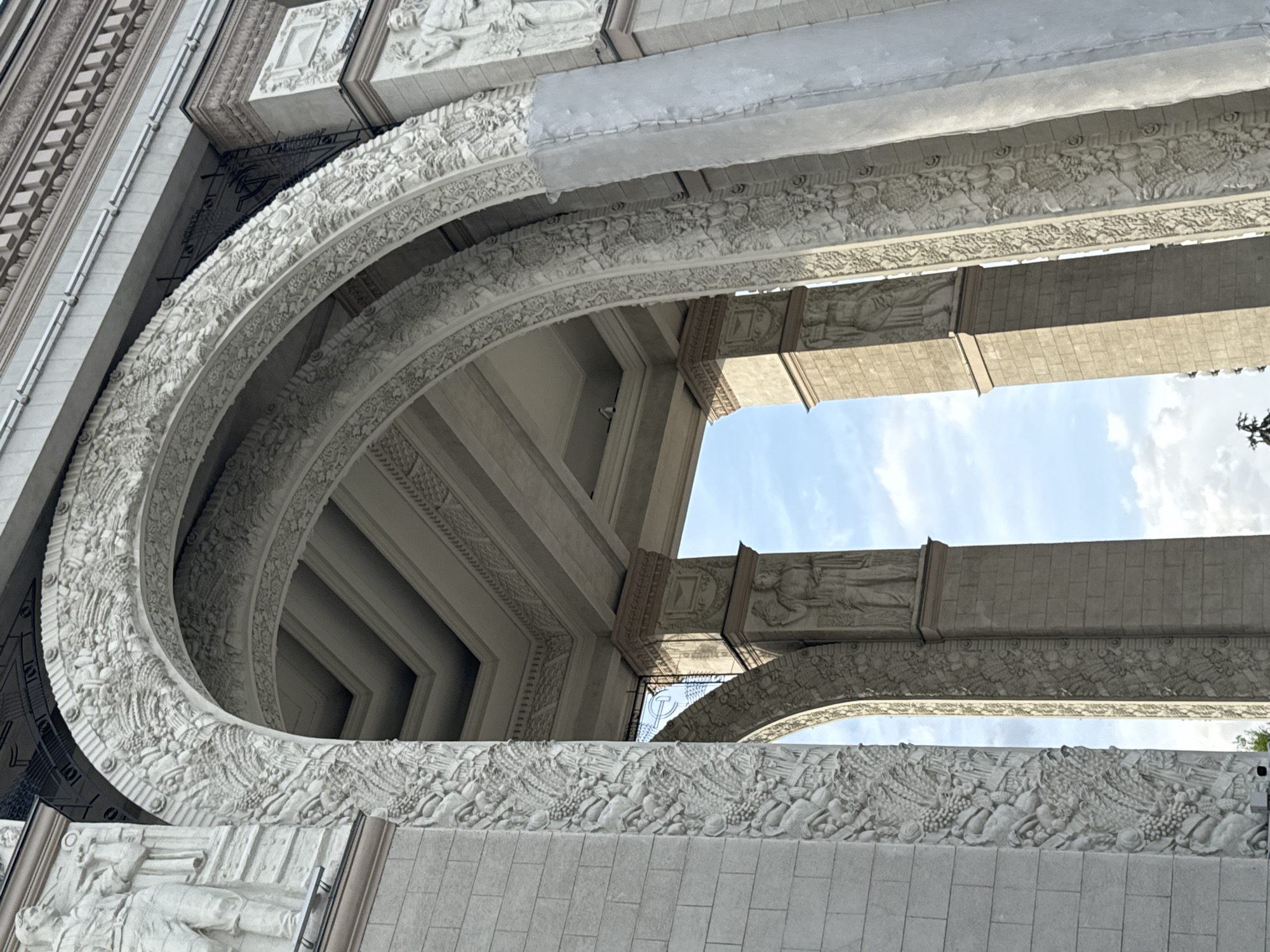 The image shows a low-angle view of an ornate, light-colored stone structure. The architectural elements include curved archways, intricate carvings of figures and foliage, and large stone blocks. The structure appears to be part of a monument or significant building. The sky is visible through openings in the structure.
Although the location in the city of Khimki, Russia, cannot be definitively determined from the image, the style of architecture resembles Soviet-era monuments often found in Russia. Without more specific information from the photograph itself, it is difficult to confirm its precise location.
