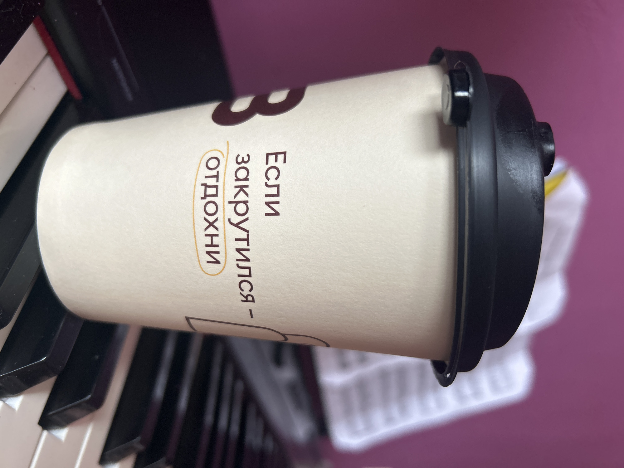 A coffee cup with Russian text "Если закрутился - ОТДОХНИ" (If you got screwed - RELAX) rests on a piano keyboard. The photo was likely taken indoors, and there are no people visible in the image. Given the Cyrillic text, it is probable that this photo was taken in Russia.