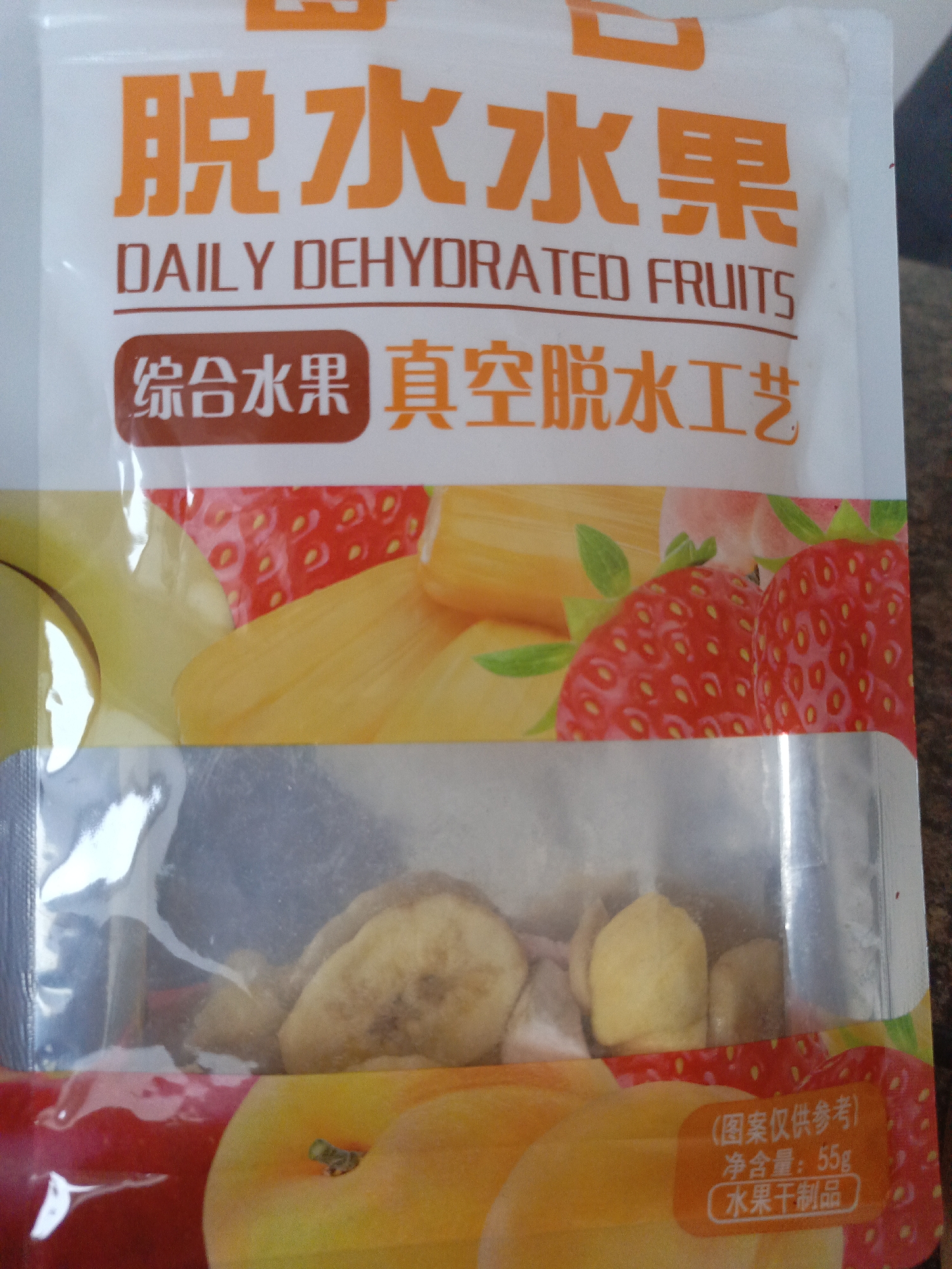 A close-up shot captures a package of "DAILY DEHYDRATED FRUITS." The Chinese characters "脱水水果" are prominently displayed above the English text. A label reading "综合水果 真空脱水工艺" is visible. Below these labels, the package features images of various fruits like apples, strawberries, and jackfruit. The clear window in the center reveals the dehydrated fruits within. The bottom right of the packaging includes another label with Chinese characters and the weight, "55g."