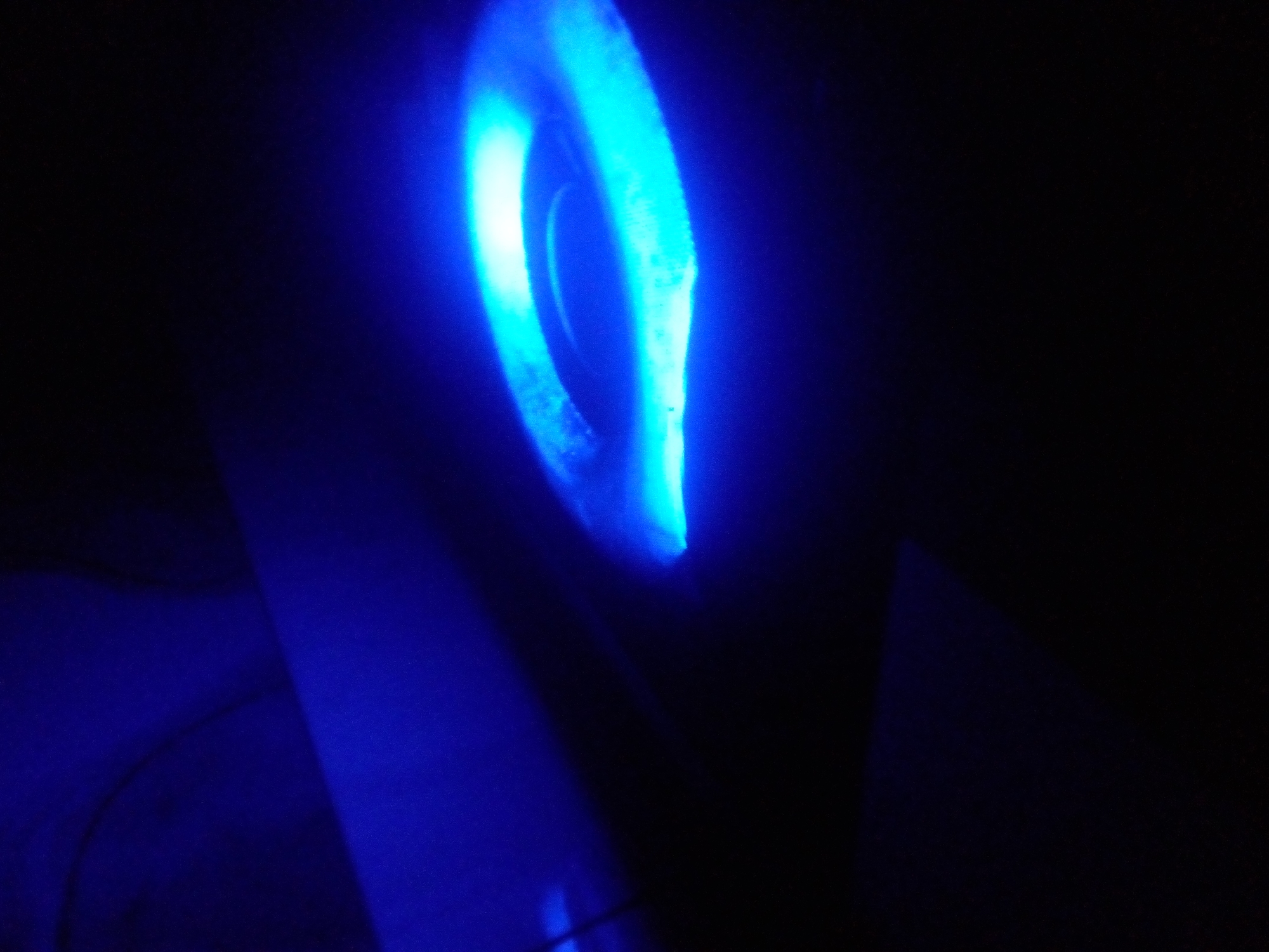 The image depicts an abstract, dimly lit scene dominated by a bright blue light source, possibly a neon tube or LED strip, which appears to be bent into a circular or oval shape. The light emanates from the object, casting a strong glow and creating a vibrant blue gradient that fades into darkness. The background is predominantly black, with subtle hints of blue light reflecting off unseen surfaces, suggesting a confined or partially illuminated space. There are no visible people, specific objects, or discernible actions taking place in the scene. The location of Nyanya, Nigeria, is not indicated by any visible elements within the image itself.