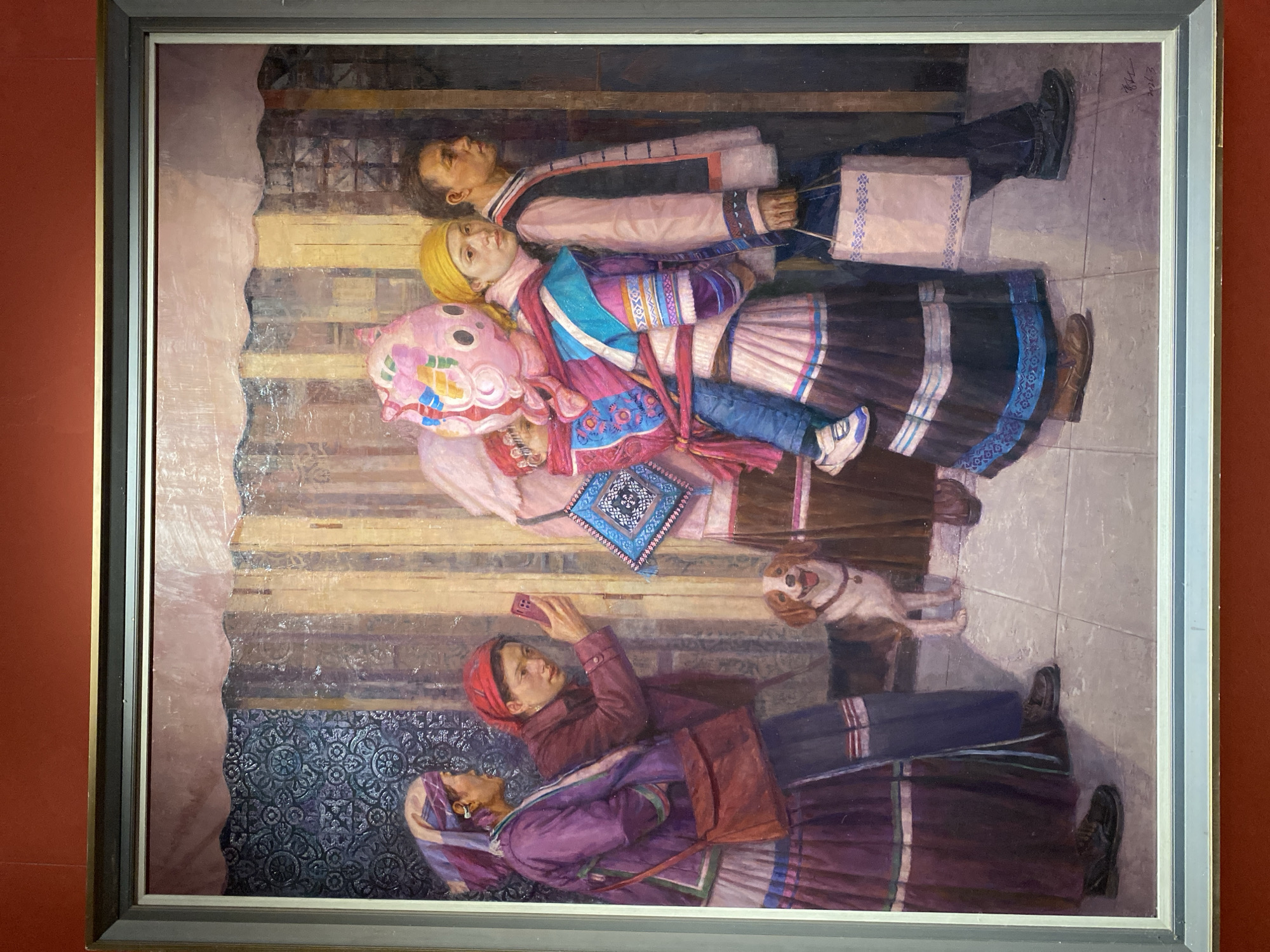 This is a painting depicting a group of people and a dog walking down a street in Yuzhong District, China. The figures are dressed in traditional clothing, with vibrant colors and intricate patterns. In the foreground, a woman carries a child on her back, the child's face obscured by a large, pink, cartoon-like headdress. To her left, a woman in a purple outfit with a headscarf is looking at her smartphone. A small, brown and white dog walks beside them. Behind the woman with the child, a man in a light-colored jacket walks with a bag in his hand. The background shows a textured wall with vertical wooden elements. The overall impression is one of a bustling street scene, with a mix of traditional and modern elements.