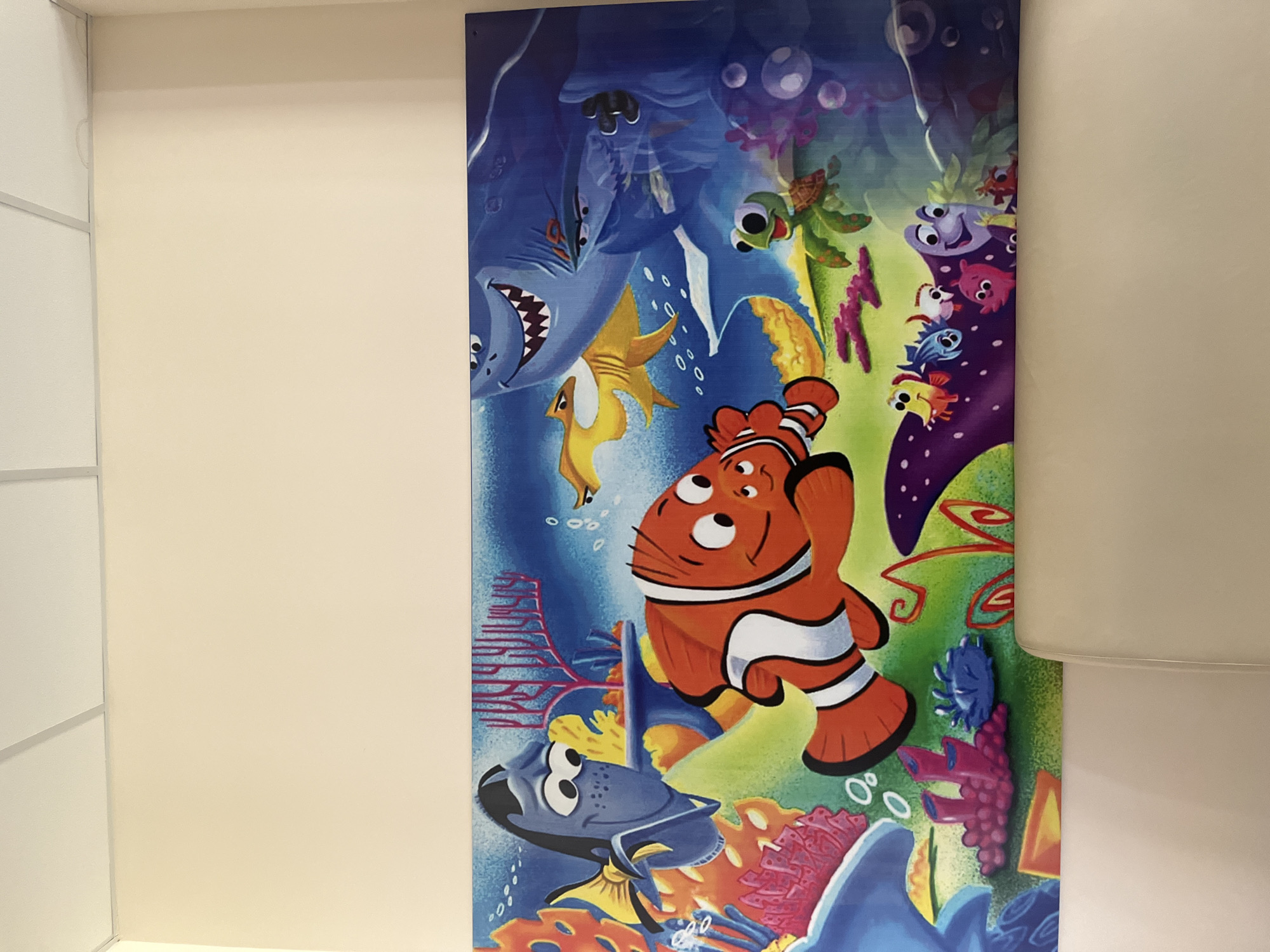 The image depicts a Finding Nemo-themed wall decoration, likely a poster or mural, installed on a cream-colored wall. The animation art showcases characters from the film, including Nemo, Dory, Bruce the shark, Crush the sea turtle, and other coral reef inhabitants. The location in Ulyanovsk, Russia, cannot be determined from the image.
