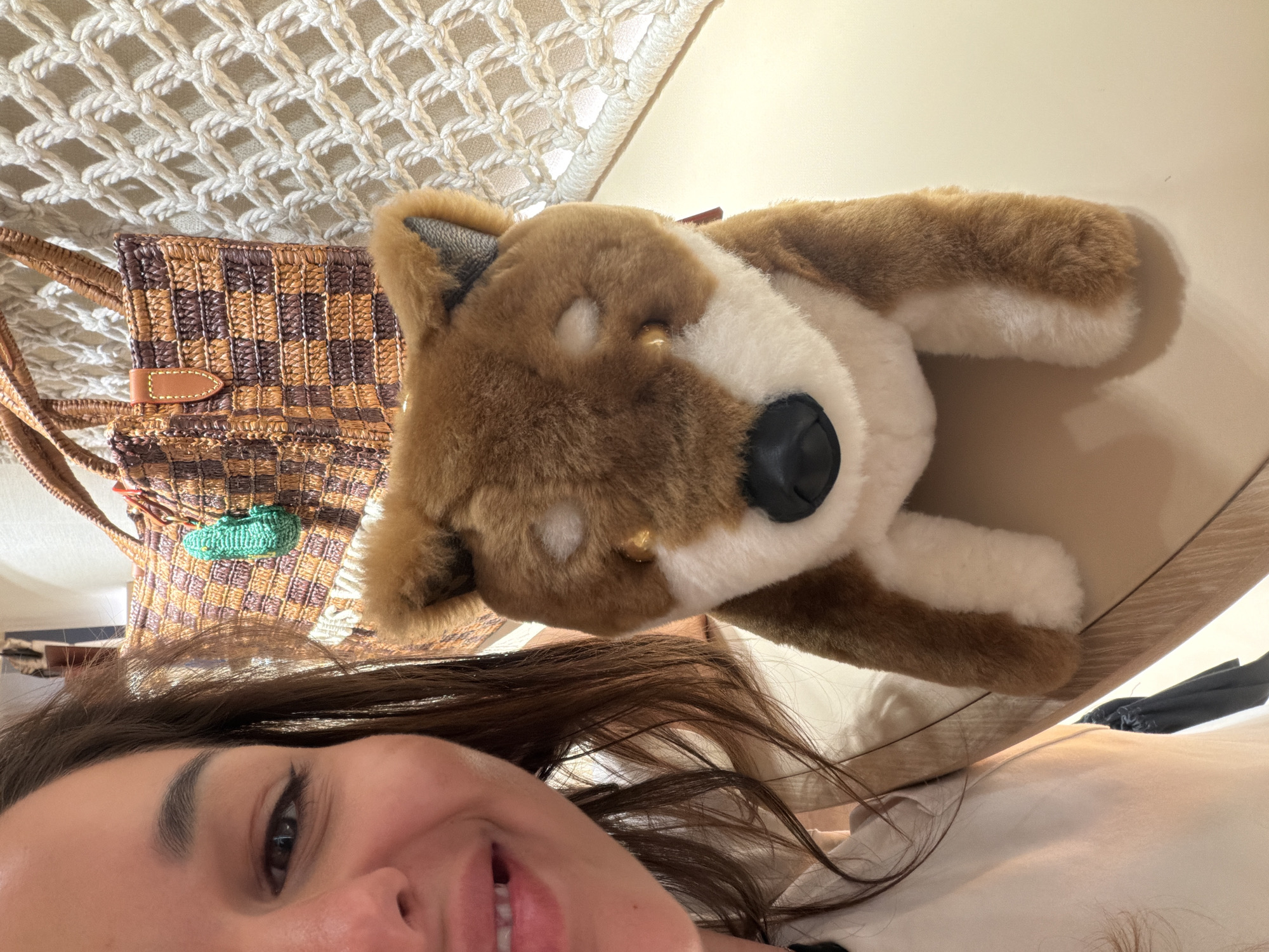 A woman is taking a selfie indoors with a stuffed dog. A checkered bag and a macrame hanging are in the background. The location is Jing'an District, China.