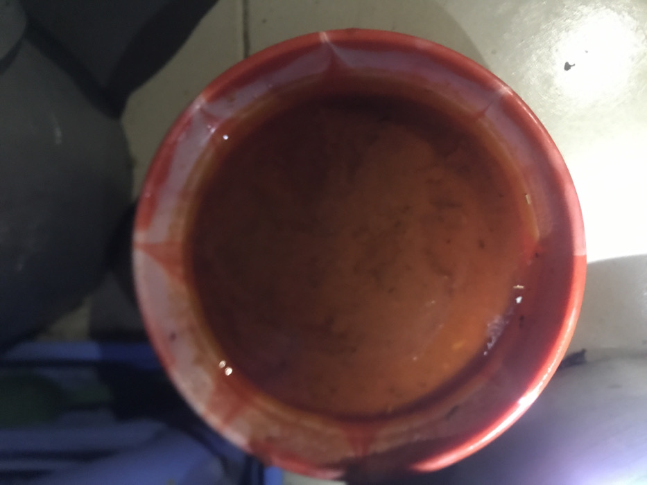 The image shows a red bowl filled with a thick, reddish-brown liquid. The bowl is made of ceramic and has a white rim. The liquid appears to be a sauce or soup. The image is taken from an overhead perspective, and the bowl is the only subject in the frame. The image was likely taken indoors. The location of the photo is in Umudike, Nigeria, based on the provided coordinates.