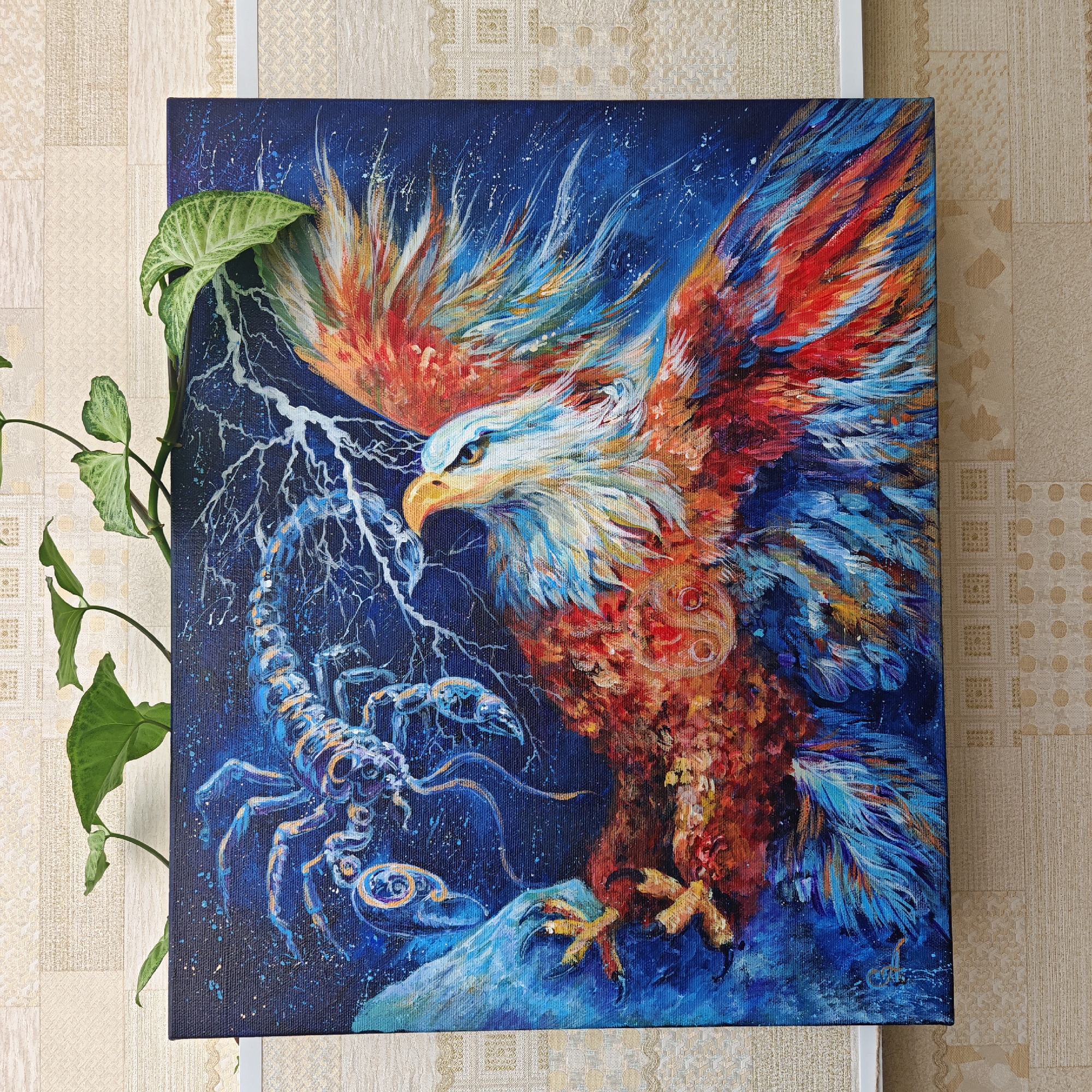 An acrylic painting of a mythical battle between an eagle and a scorpion hangs on a wall. The eagle, with red, orange, and white feathers, is painted in an expressive, almost abstract style. The eagle has a sharp, piercing gaze, staring down at a scorpion. The scorpion, rendered in shades of blue and white, sits beneath the eagle. The background is a dark blue sky with painted white lines representing lightning bolts. A green plant sits adjacent to the painting. The wall behind the painting has a subtle beige pattern. The location is Taganrog City District, Russia.