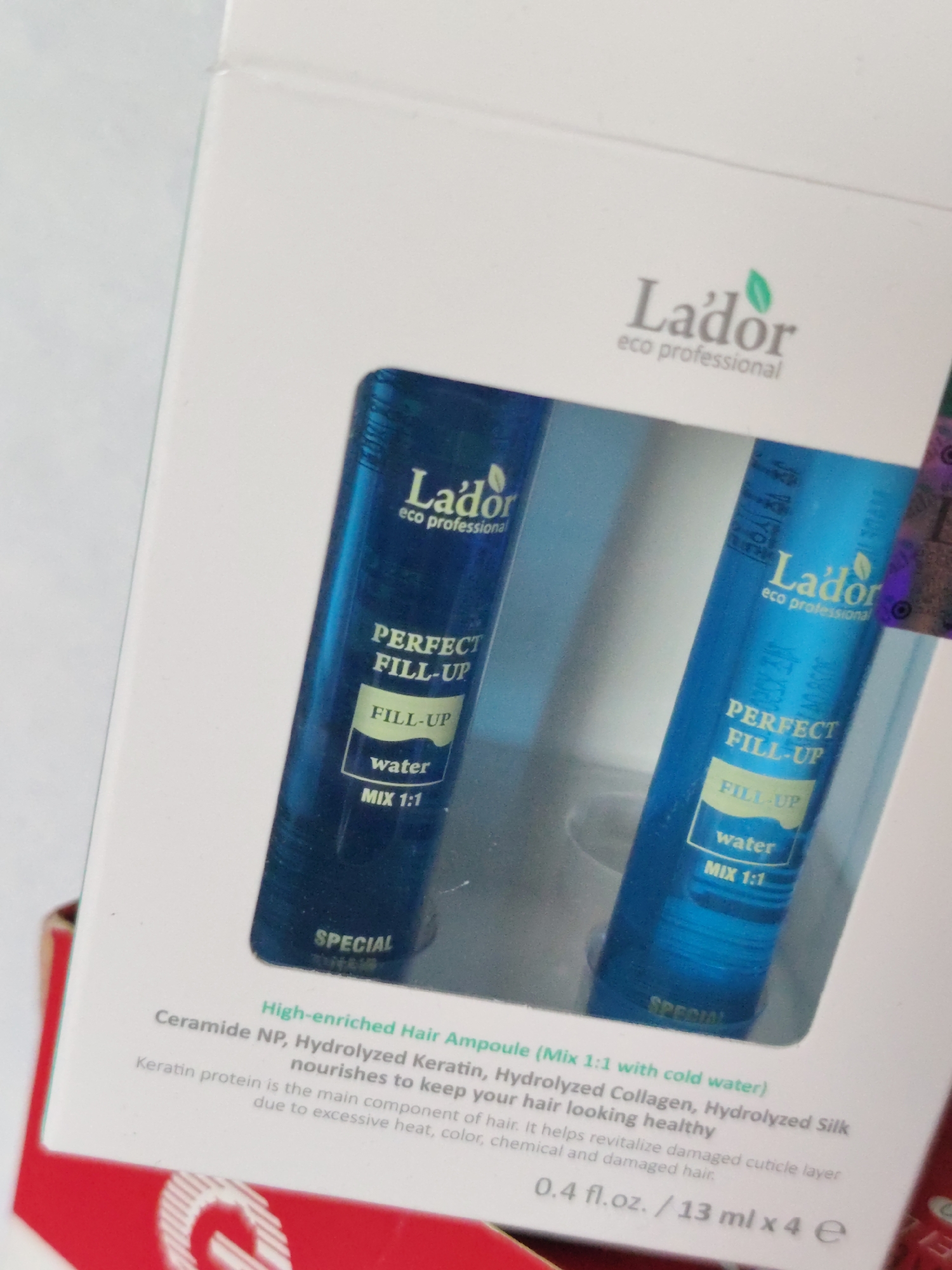 The image shows a white box containing two blue vials of L'ador Perfect Fill-Up hair treatment. The box is angled, and the vials are partially visible through a clear window. The L'ador logo, a stylized leaf above the brand name, is visible on the box and on the vials. Text on the vials indicates "PERFECT FILL-UP", "water", and "MIX 1:1". Smaller text on the box describes the product as a "High-enriched Hair Ampoule". The image does not provide any information about the location in Mykolaiv, Ukraine.