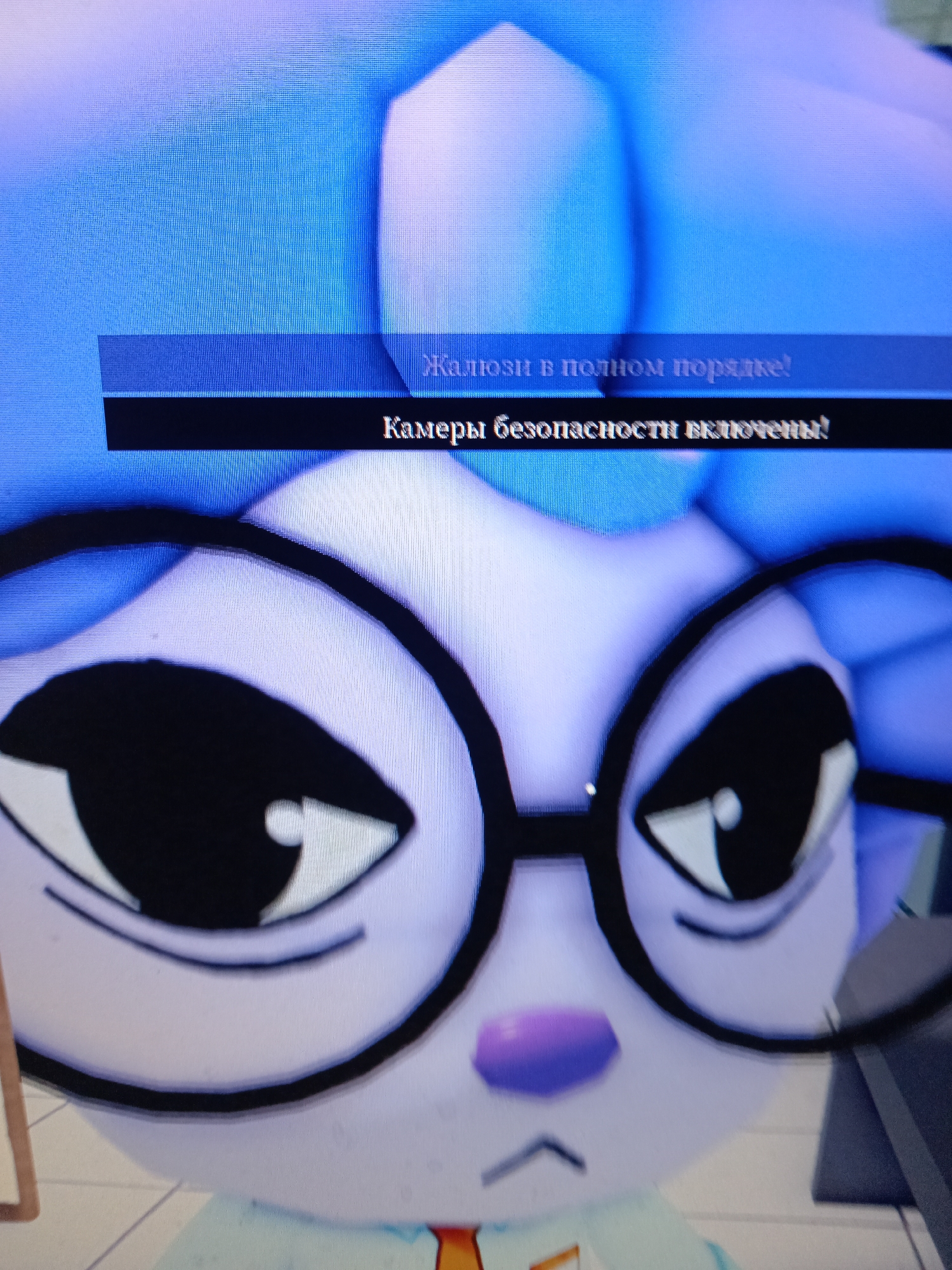 The image shows a close-up of a cartoon character wearing glasses. The character appears to be a white, anthropomorphic animal with large black eyes and a purple nose. Text is visible in the upper portion of the image, appearing to be part of a game or application interface. One line of text, in a lighter font on a blue background, reads "Жальзи в полном порядке!" (Zhalzi in full order!). Below this, on a black background, is text in white font that reads "Камеры безопасности включены!" (Security cameras are enabled!). The overall aesthetic is bright and digital, suggesting a screen display. There is no discernible connection to the city of Rudny, Kazakhstan, or any specific real-world location. The image depicts a digital representation of a character and accompanying text, likely from a video game or animated media.