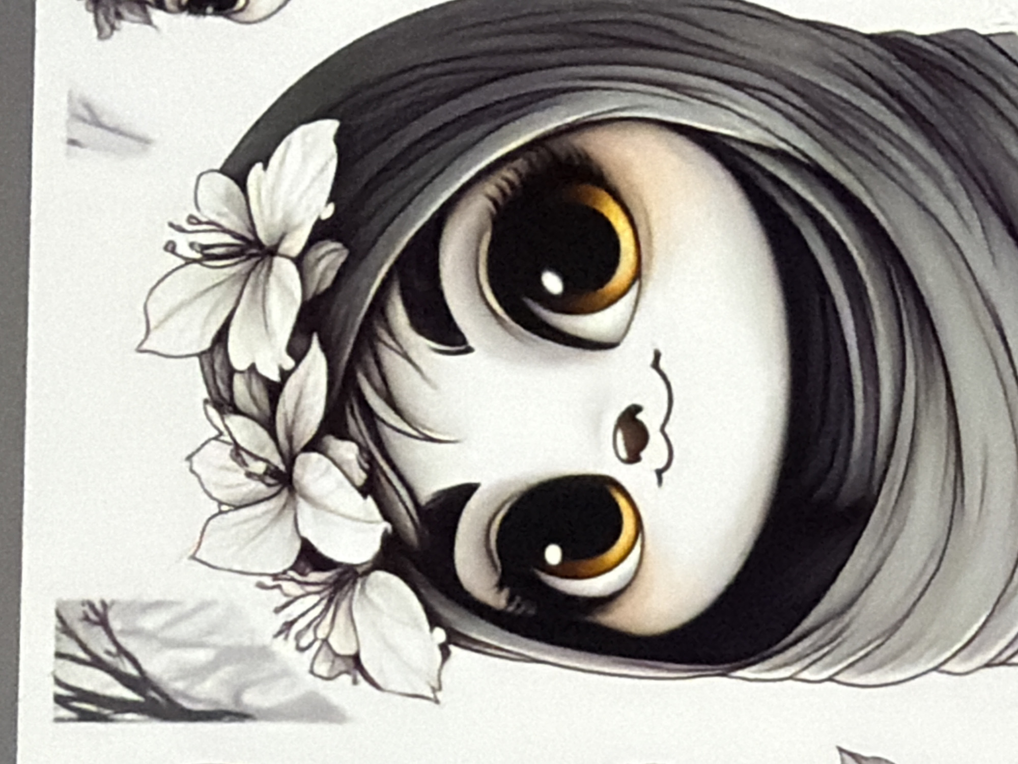 A stylized, digitally rendered illustration features a cute, anthropomorphic character presented against a plain white background. The character has a pale white face with large, prominent, round eyes. The eyes feature sizable, dark pupils encircled by a vibrant golden-yellow iris, each containing a small, bright white circular highlight. Delicate, dark eyelashes are visible along the upper eyelids. A small, dark, round nose is positioned centrally, above a thin, upward-curving line forming a subtle smile. Dark, fine strands of hair emerge from beneath a dark grey, draped head covering that frames the character's face. Adorning the head covering is a circlet of three prominent white flowers, each with a dark center and subtle grey shading; two are fully visible, while one on the left is partially cropped. The head covering itself consists of layered folds of dark and light grey fabric that extend downwards, obscuring the rest of the body. In the upper left corner of the frame, a partial, grayscale depiction of bare tree branches is visible against the white background.
